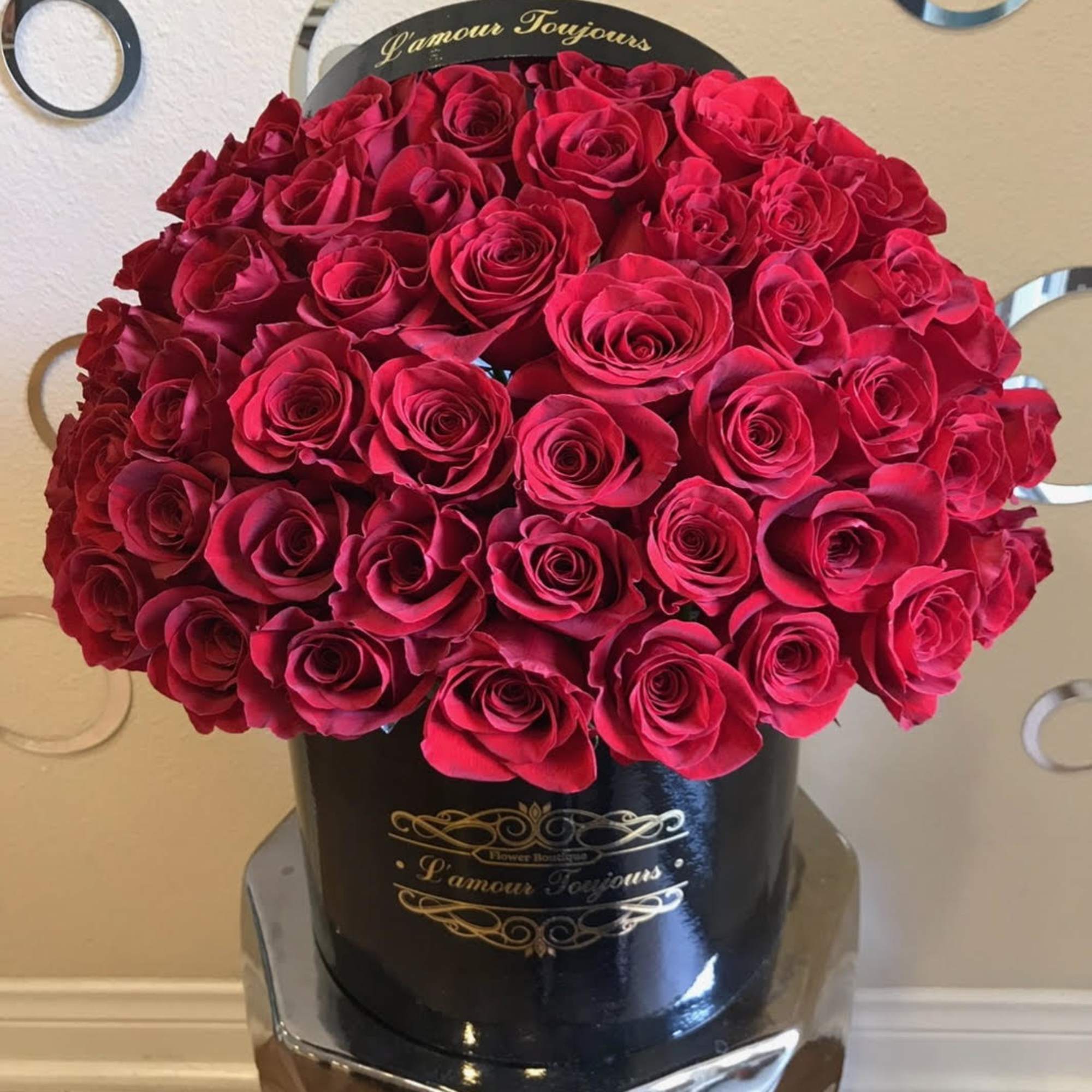 Large round box of tightly packed red roses in a black hatbox-style container with gold script