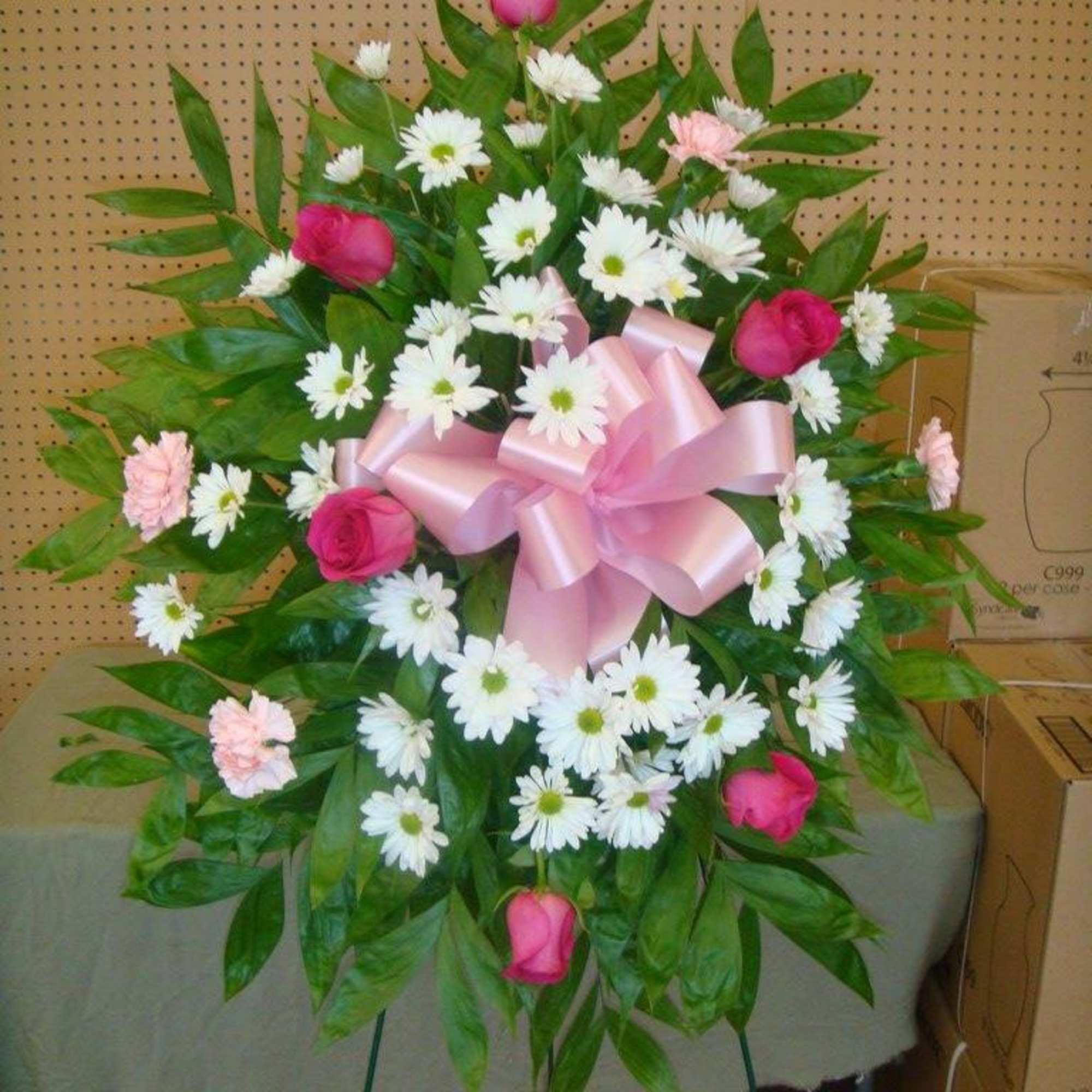 Standing floral spray with pink roses, white daisies, and a pink bow
