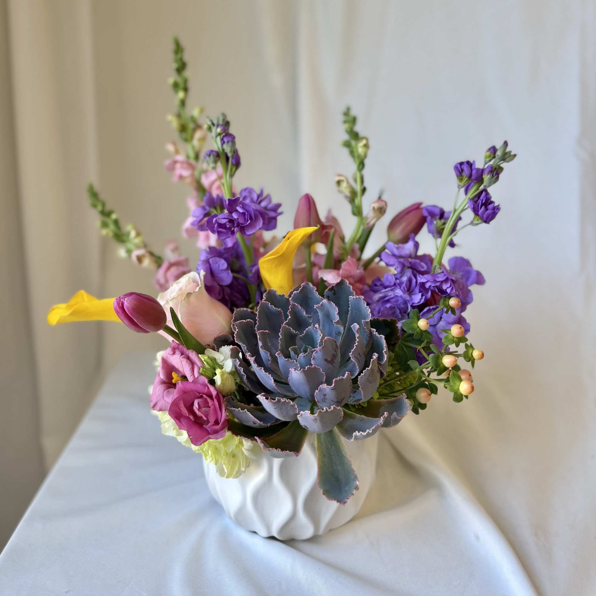 A unique arrangement filled with vibrant flowers and a live succulent, the