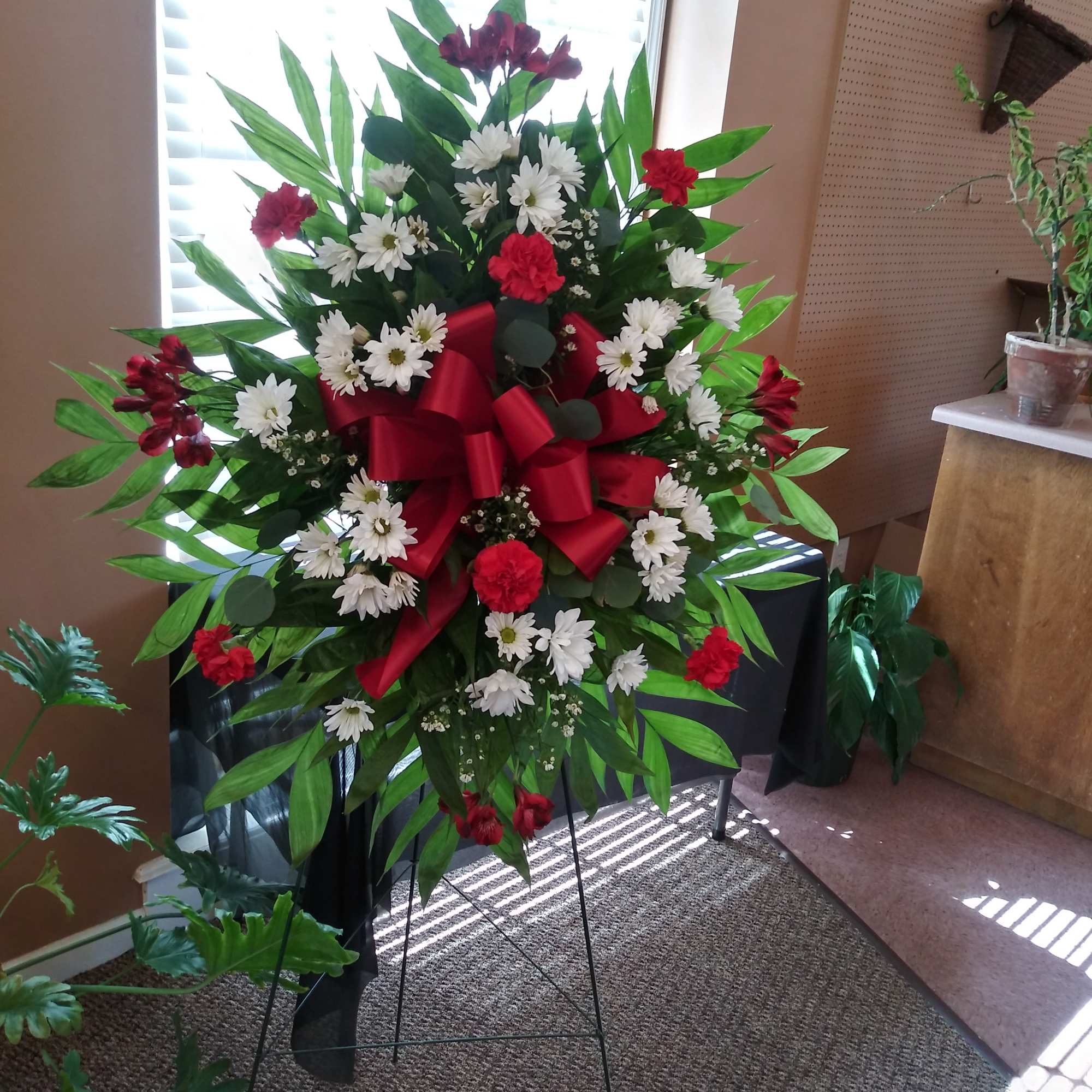Standing floral spray with white daisies and red carnations on an easel
