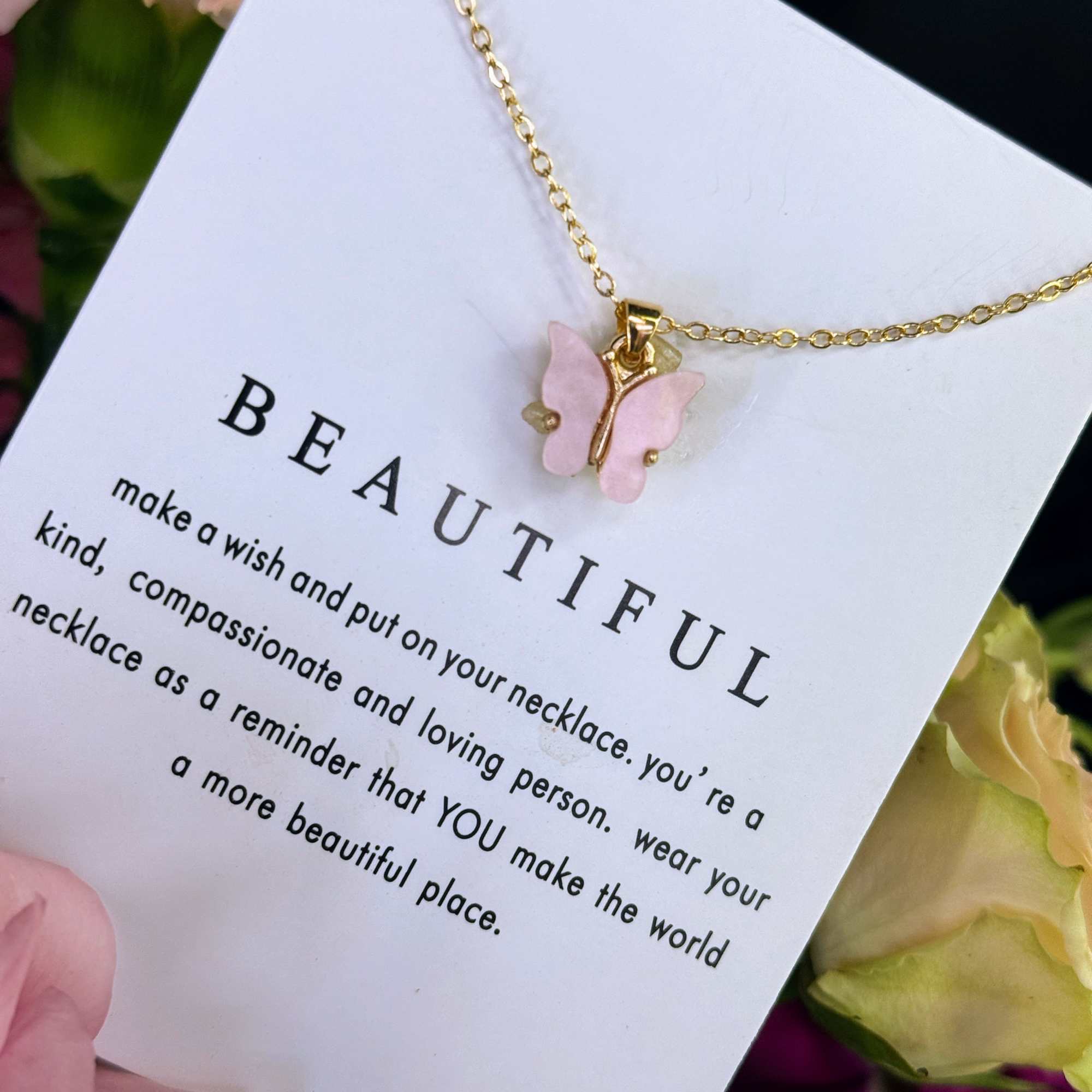 Gold butterfly necklace on a card with flowers in the background
