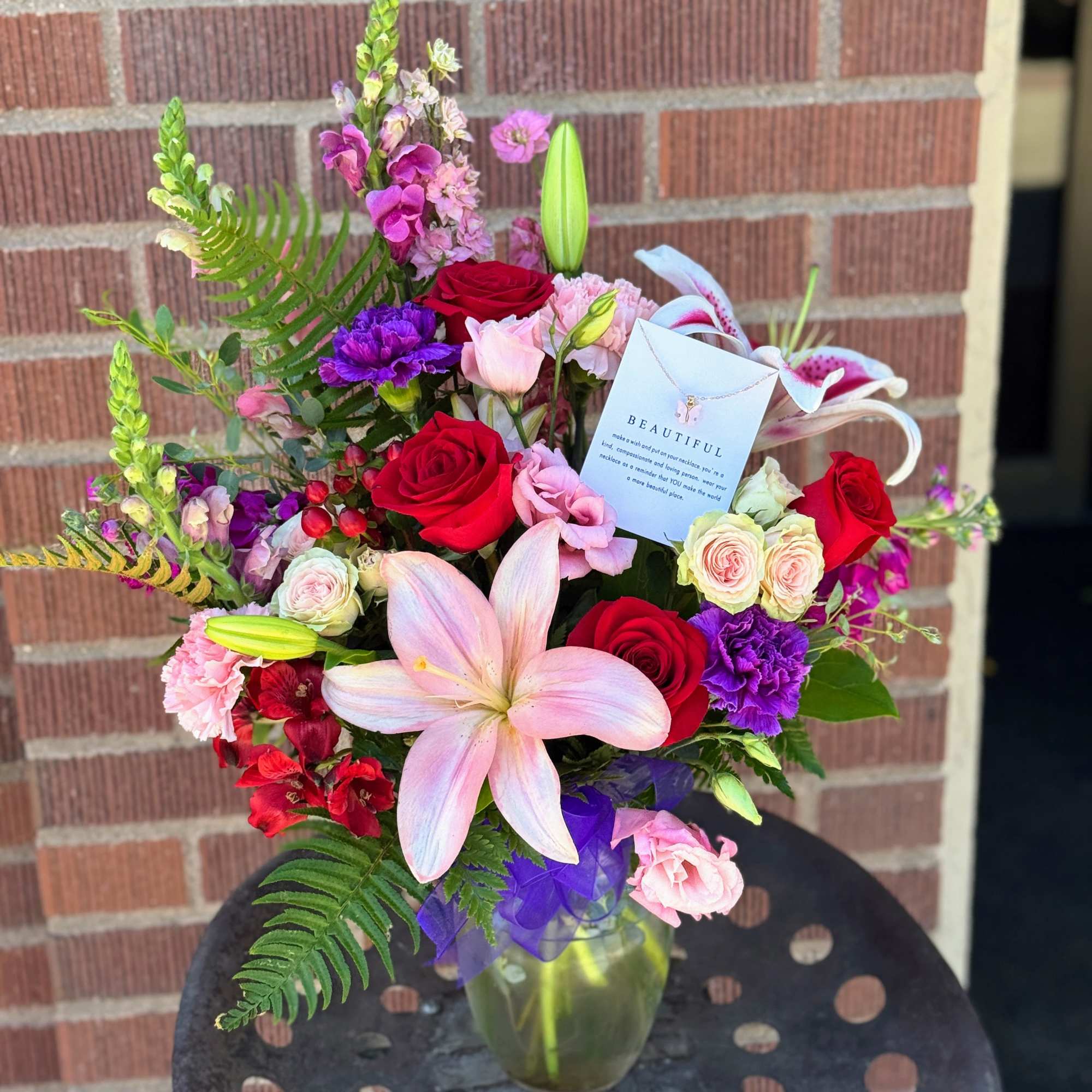 Mixed bouquet of roses, lilies, and pink blooms in a glass vase