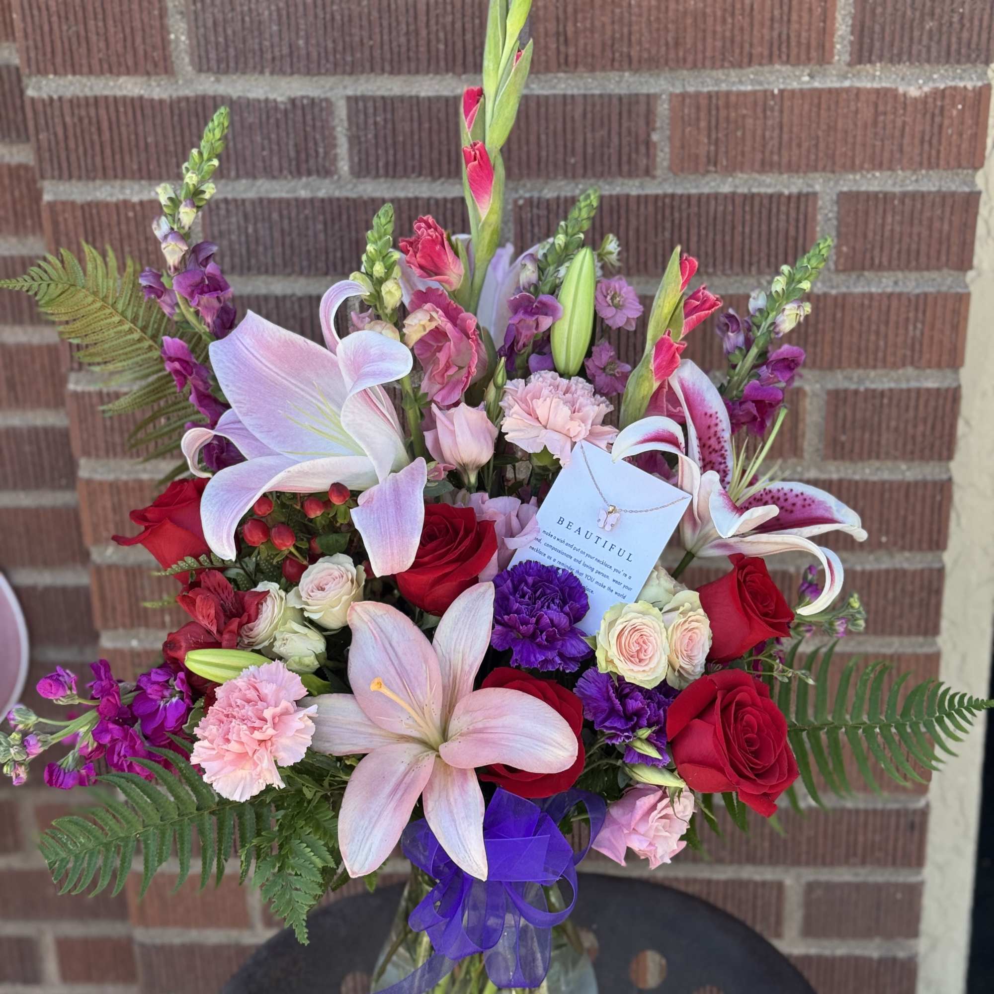 Mixed bouquet of lilies, roses, and carnations in a glass vase with a purple ribbon