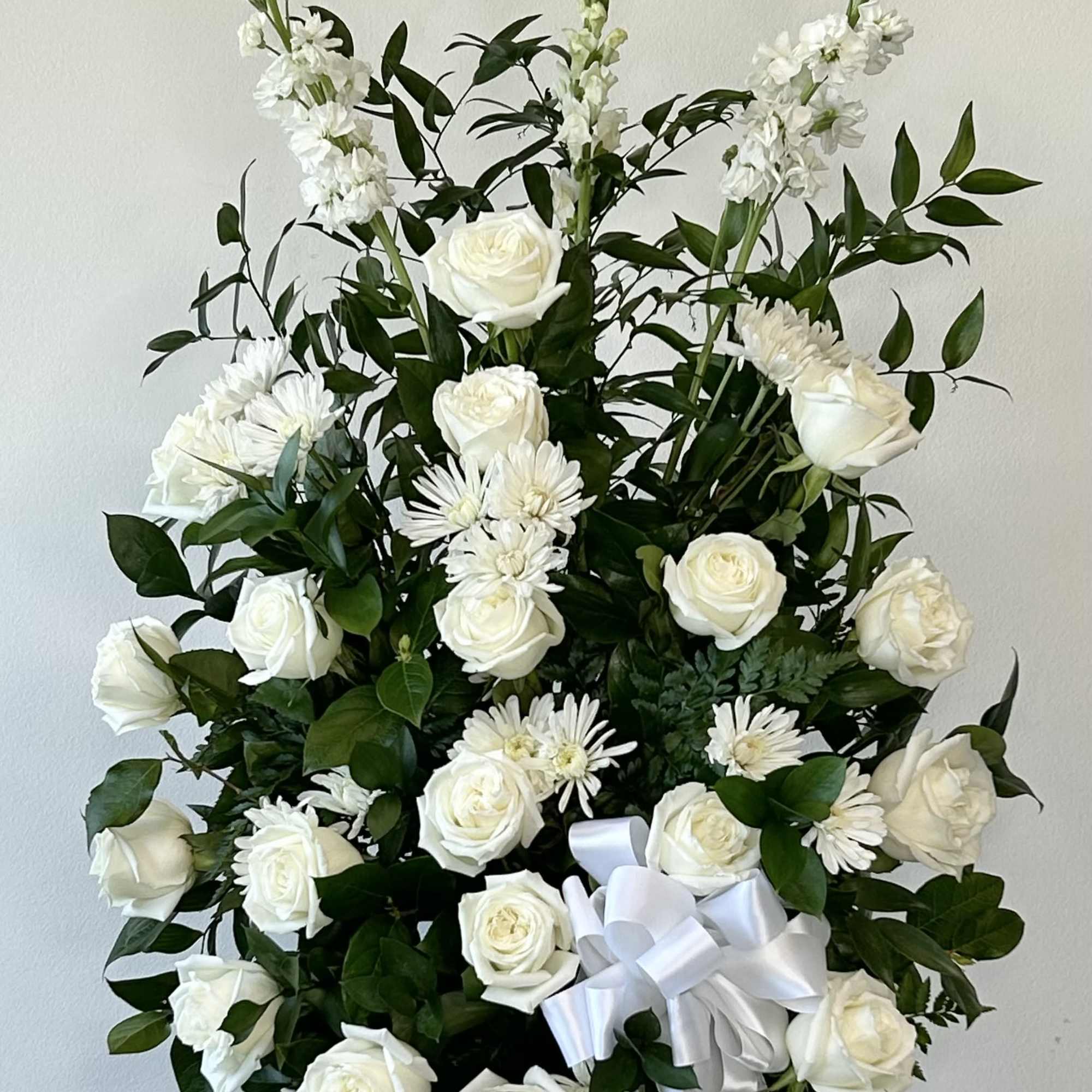Tall white floral spray with roses and daisies, finished with a white ribbon