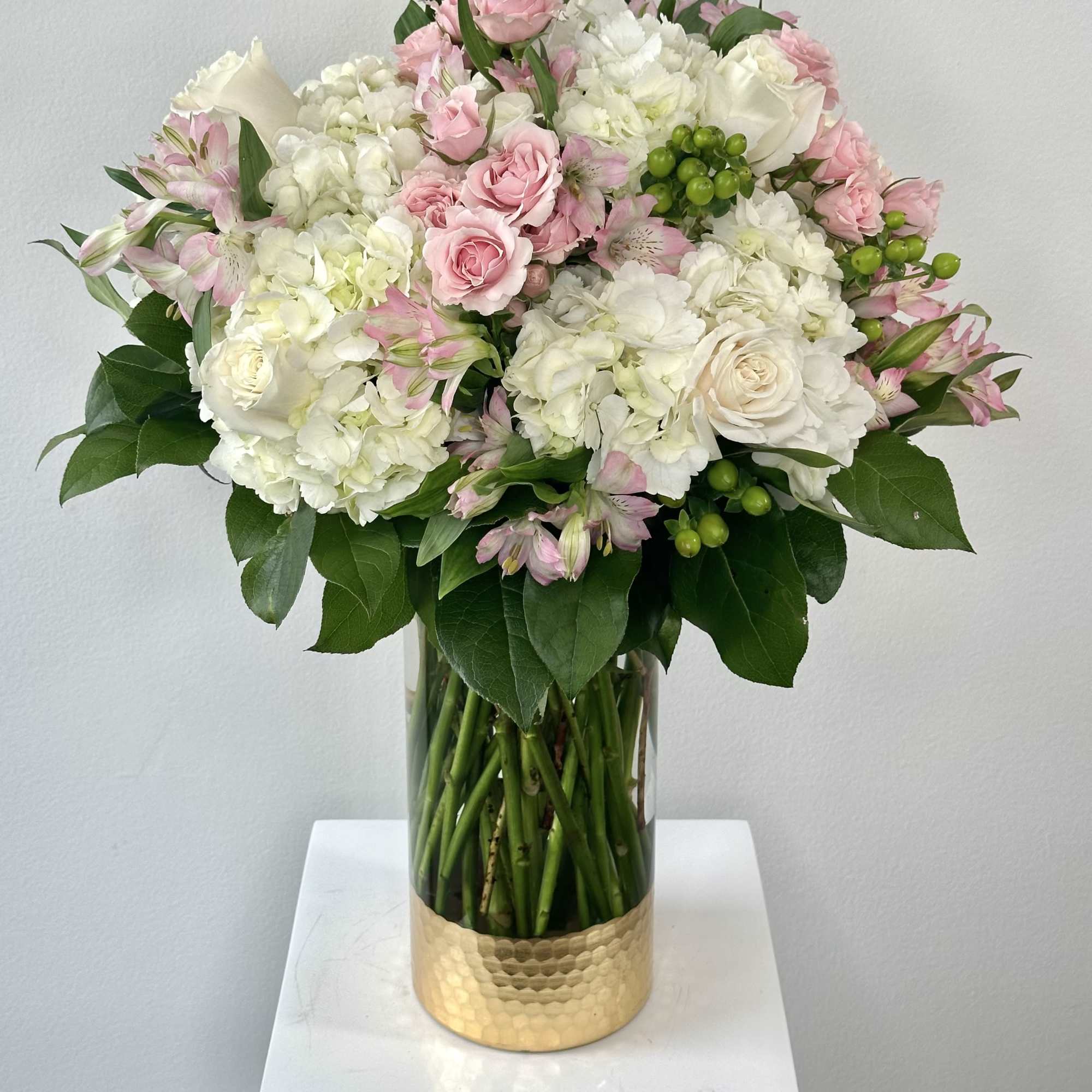 Pink and white bouquet in a clear glass vase with a gold base