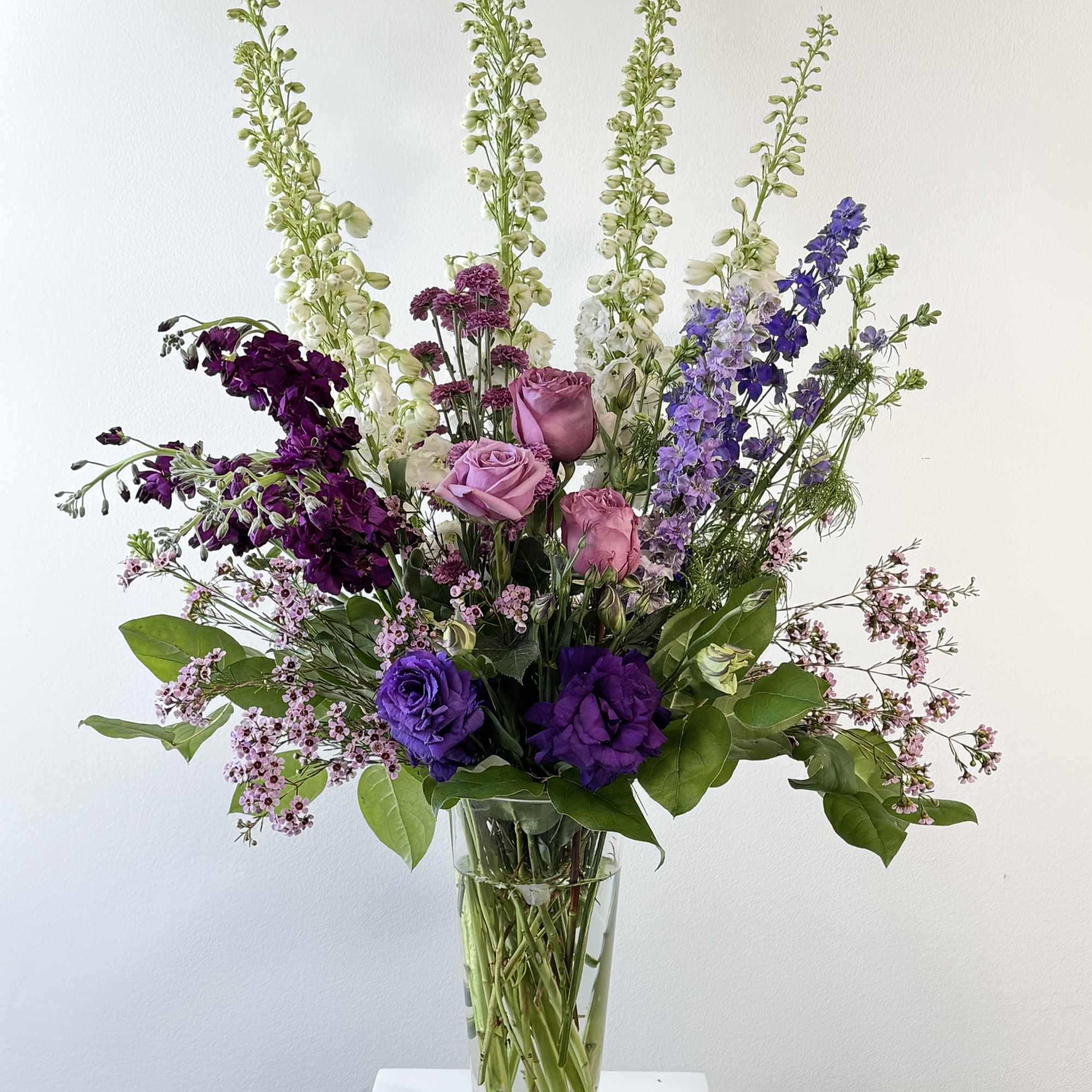 Tall mixed bouquet of purple, pink, and white flowers in a clear glass vase