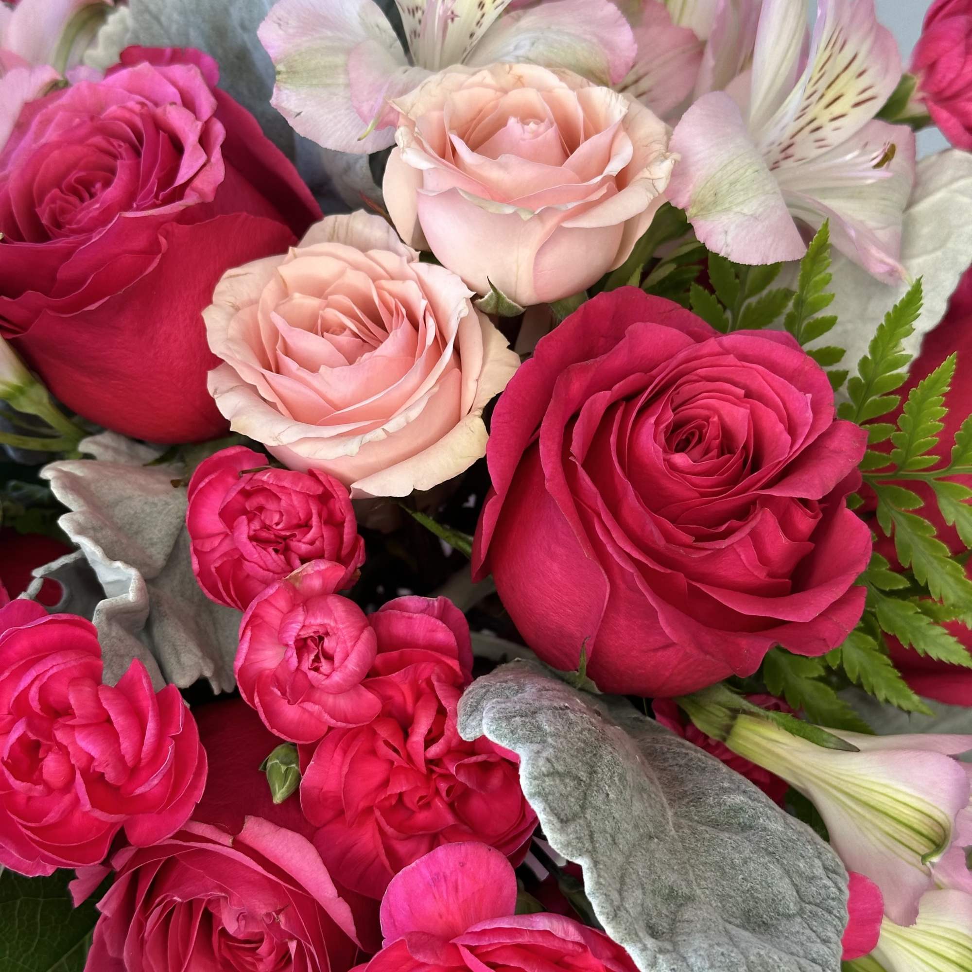 Close-up of a bouquet with hot pink and blush roses, pink spray roses, and pale pink alstroemeria blooms.