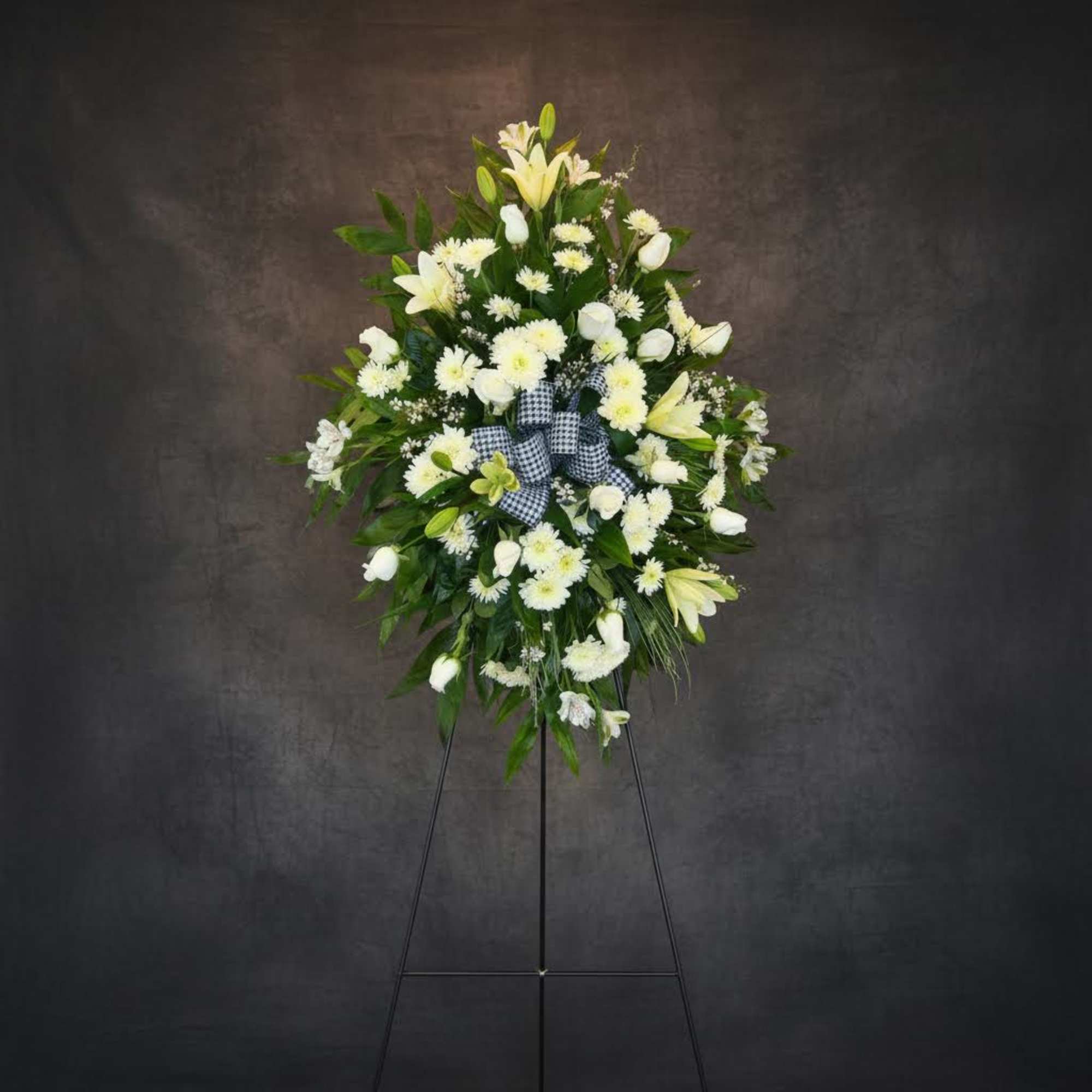 White floral standing spray on an easel with a checkered ribbon