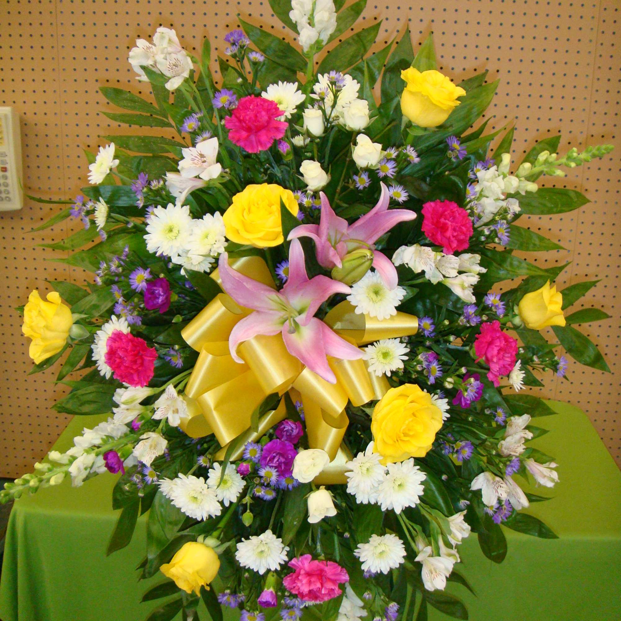 Large mixed floral spray with pink lilies, yellow roses, and a gold ribbon