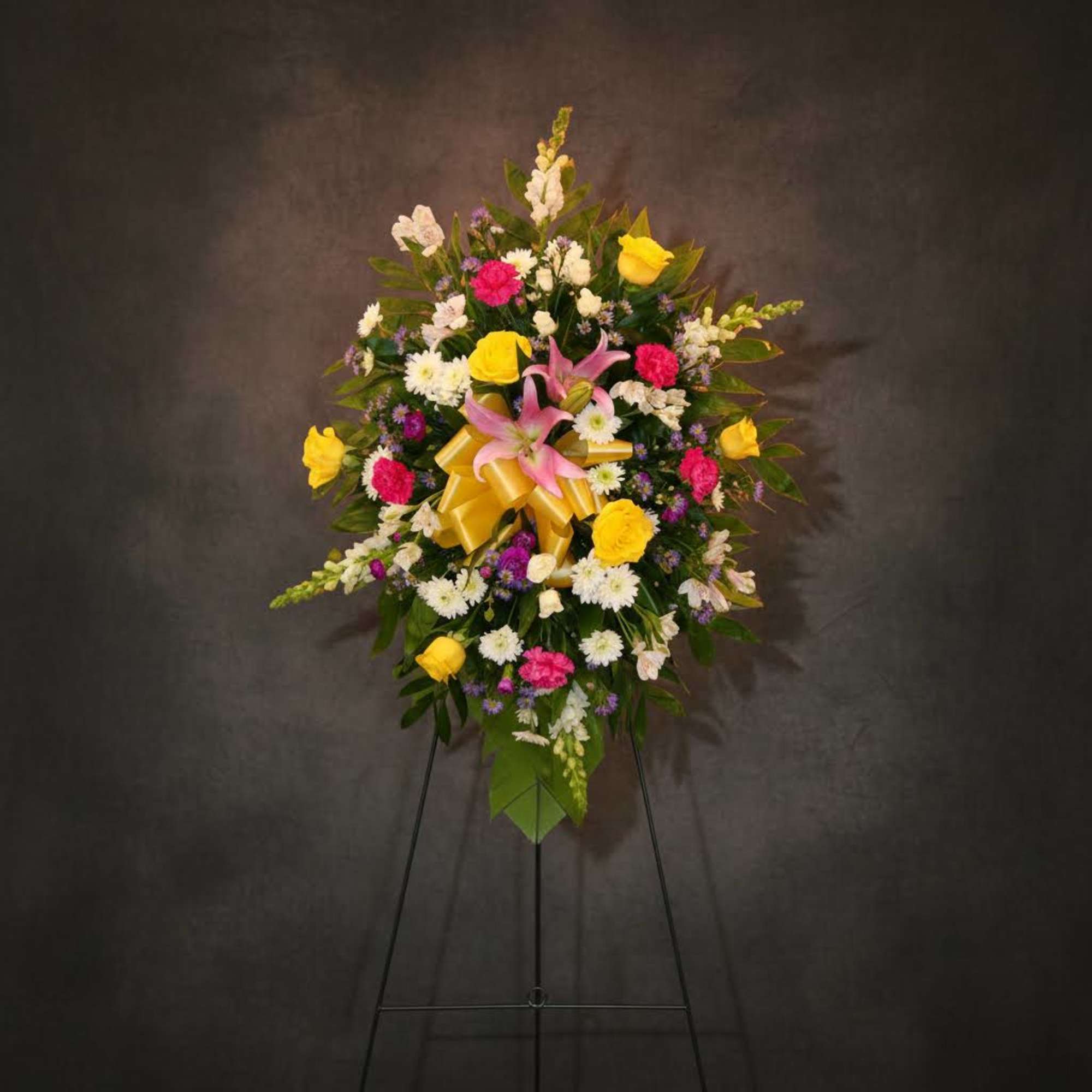 Standing floral spray with pink lilies, yellow roses, and a gold ribbon on an easel