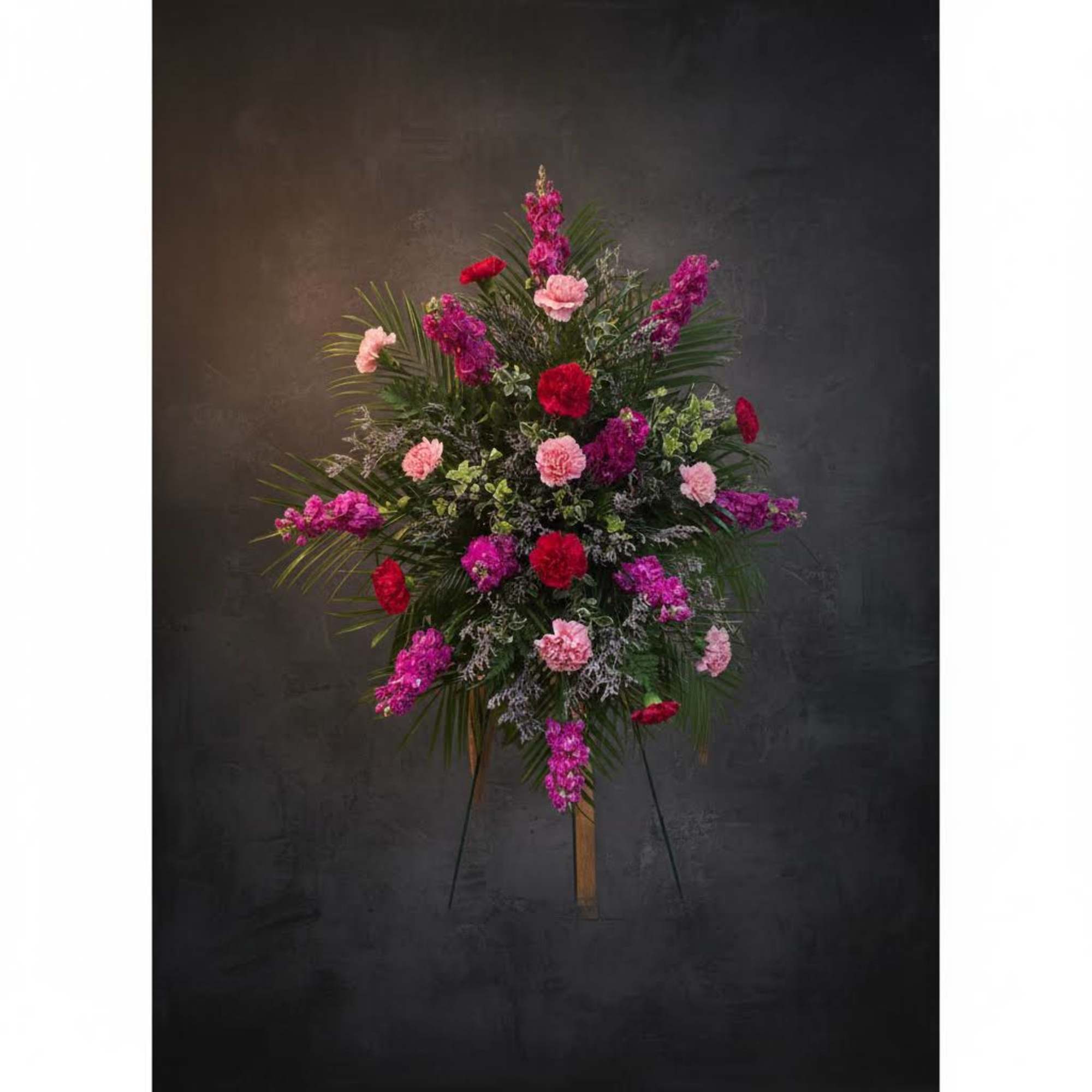 Tall standing floral spray with pink and red carnations on a dark background