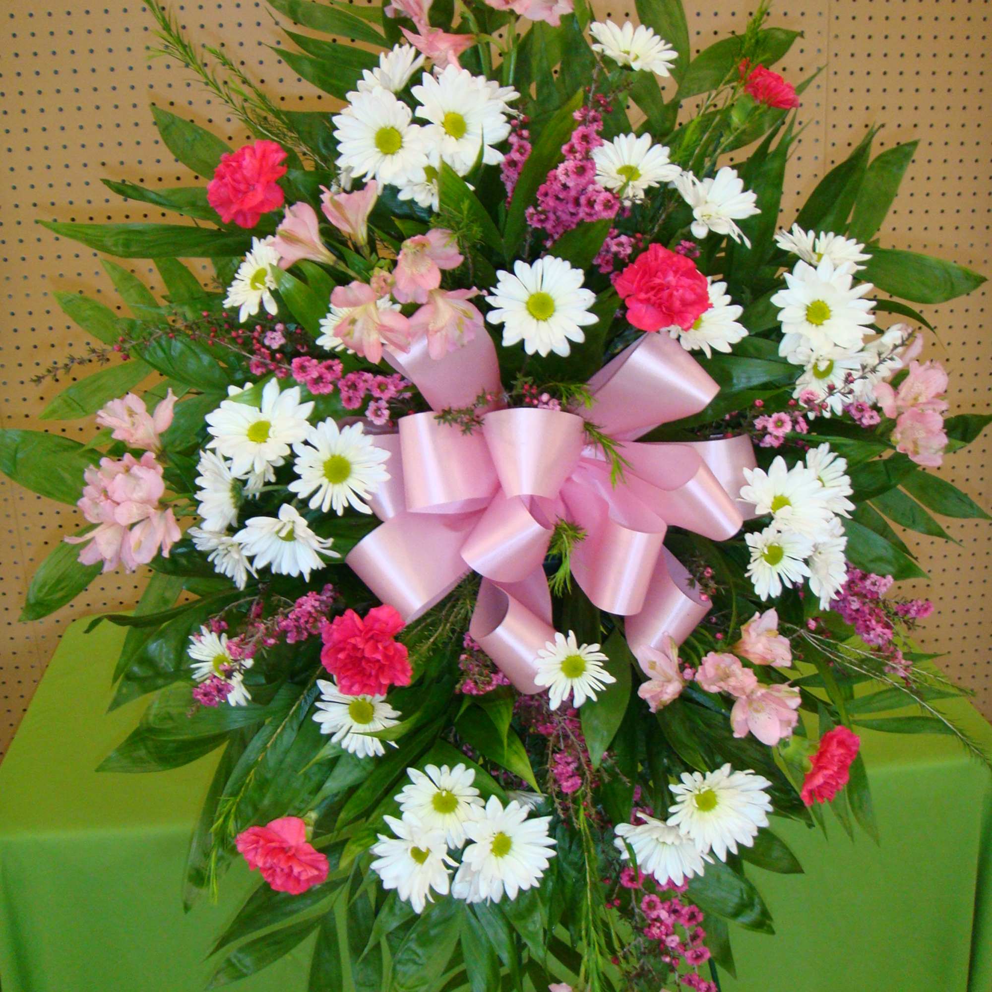 Standing floral spray with white daisies, pink flowers, and a pink ribbon bow