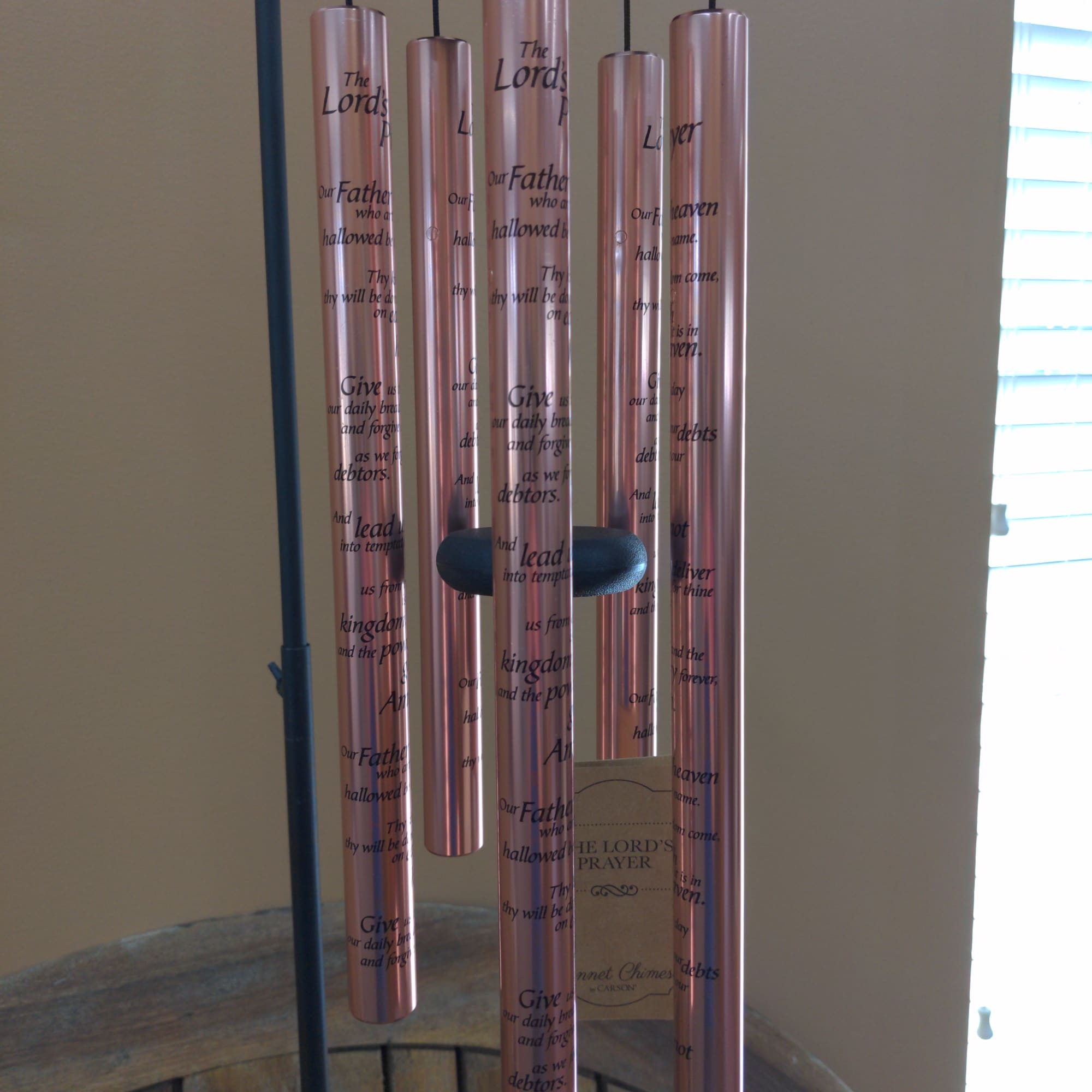 Copper wind chime with engraved prayer text hanging indoors