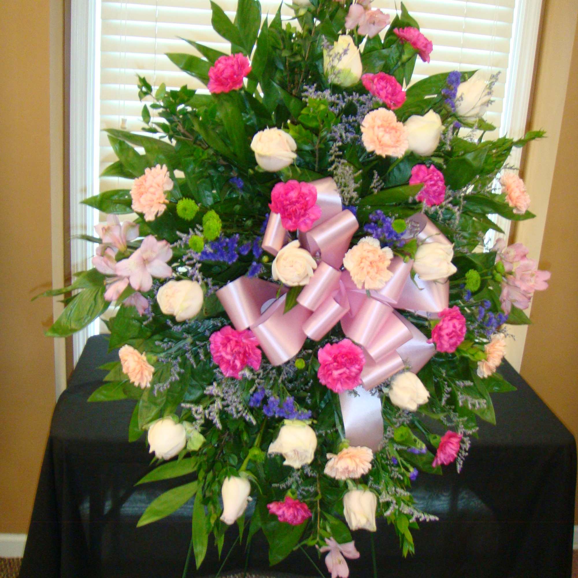 Large standing floral spray with pink, white, and peach blooms and a pink ribbon