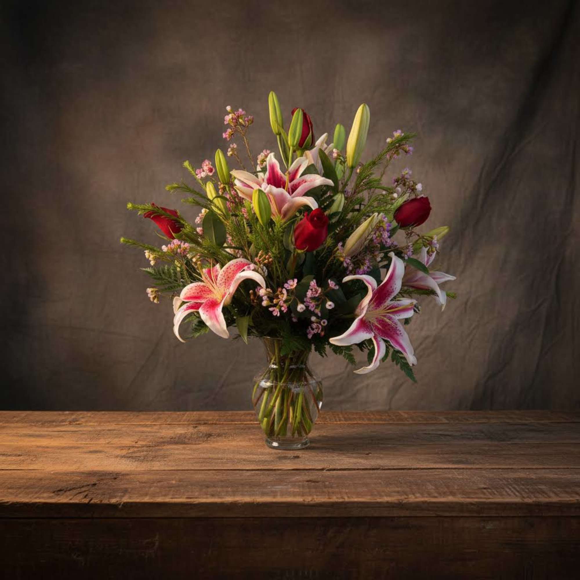 Bouquet of pink lilies and red roses in a clear glass vase