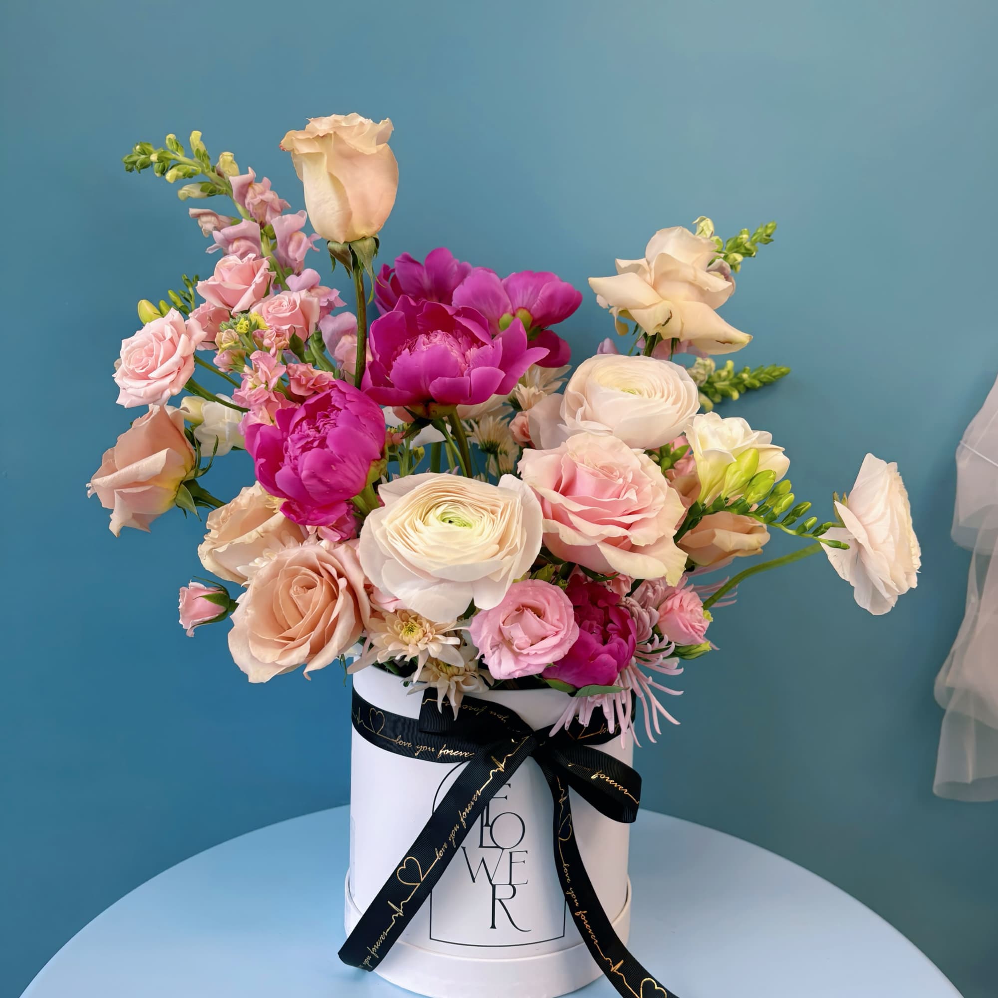 Pink and cream mixed flowers arranged in a white hat box with a black ribbon