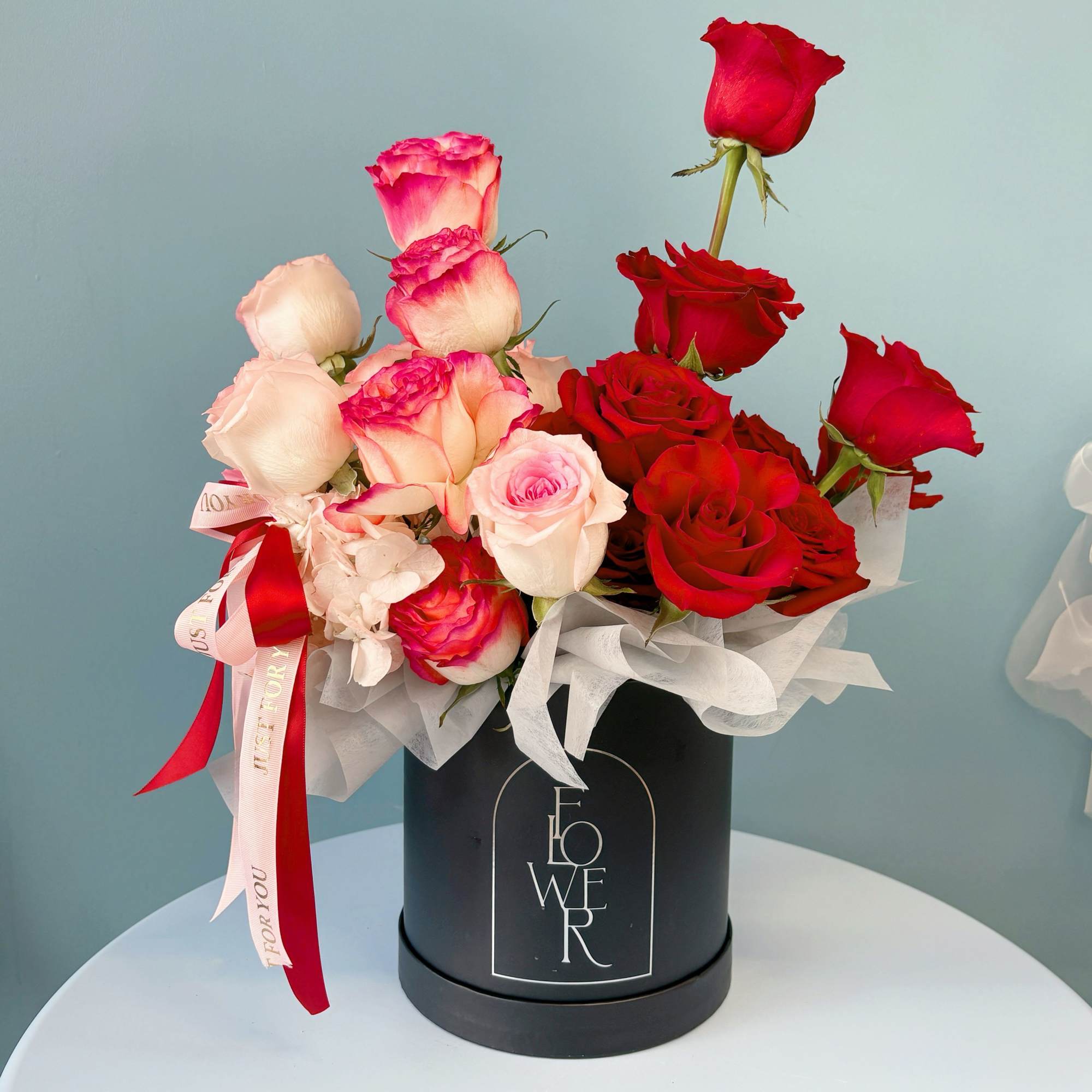 Red and blush roses arranged in a black hat box with ribbon