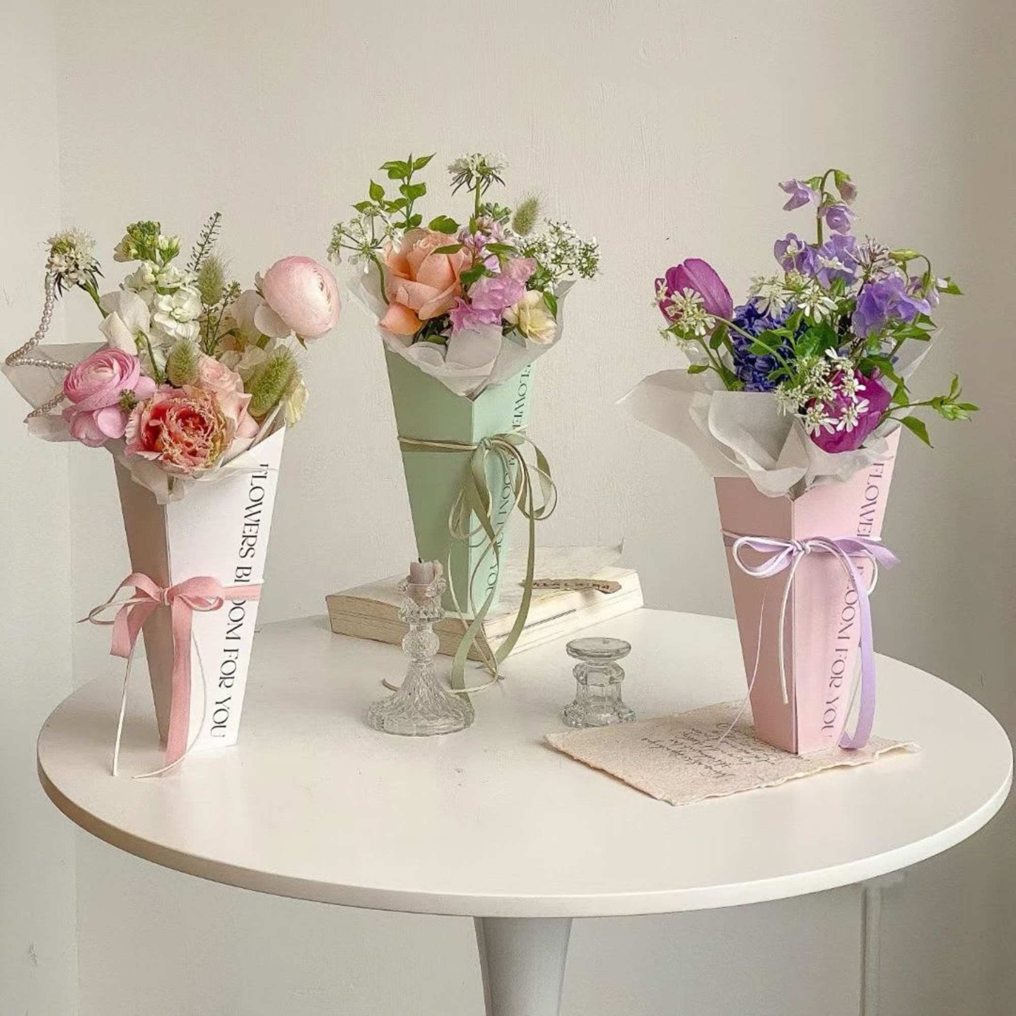 Three small pastel flower bouquets in tall gift boxes on a round table
