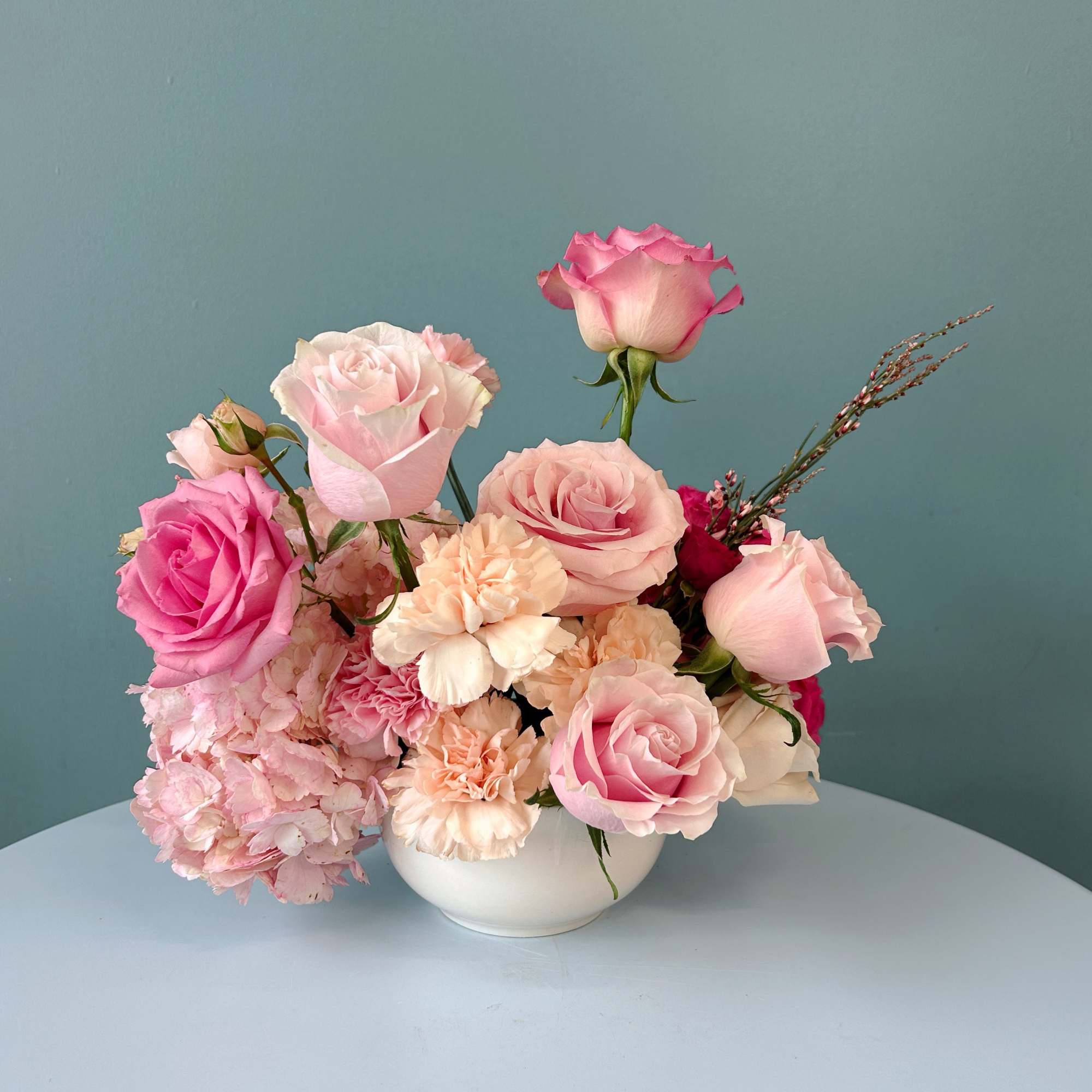 Pink and blush roses with carnations in a white bowl vase