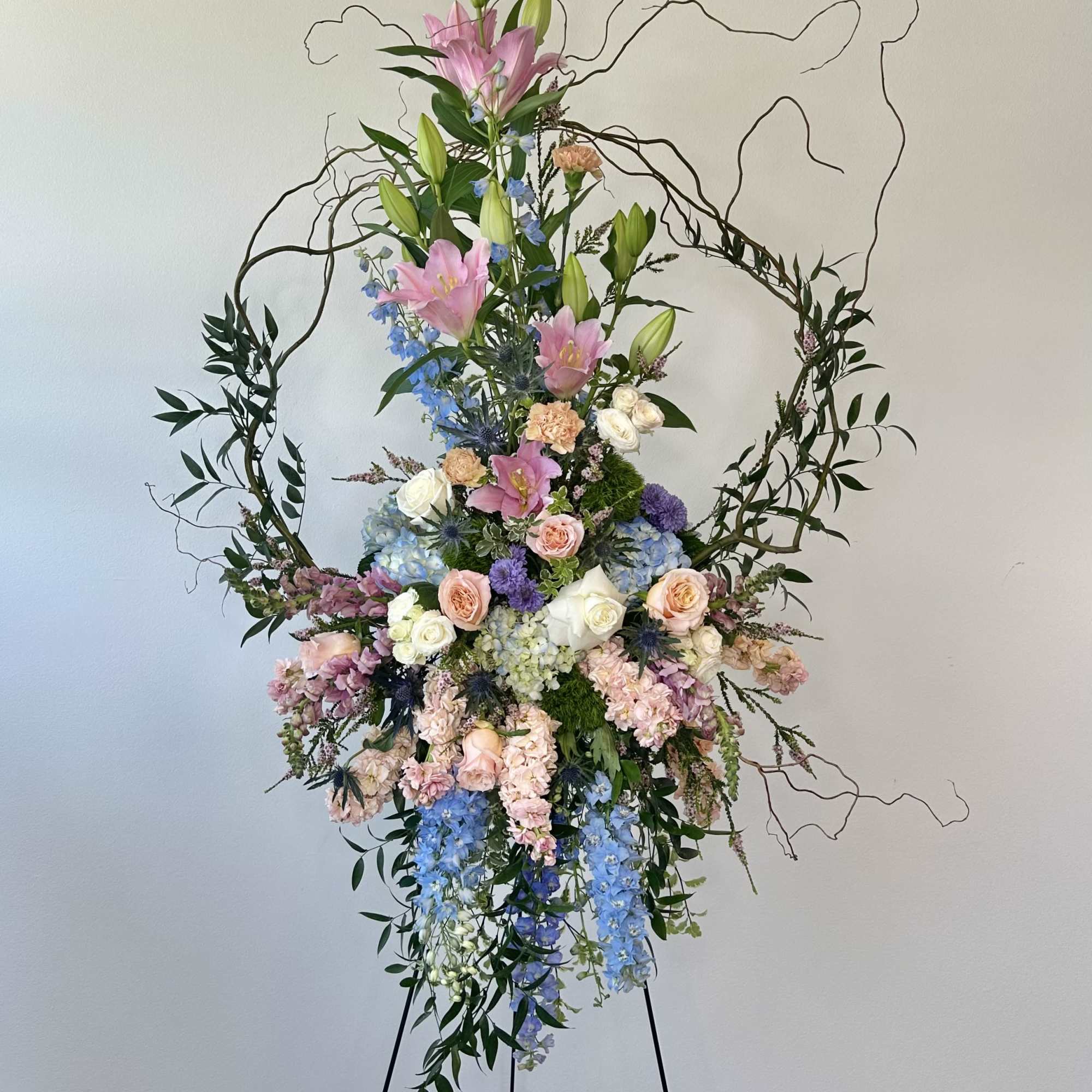 Tall floral standing arrangement with pink lilies, roses, and blue blooms