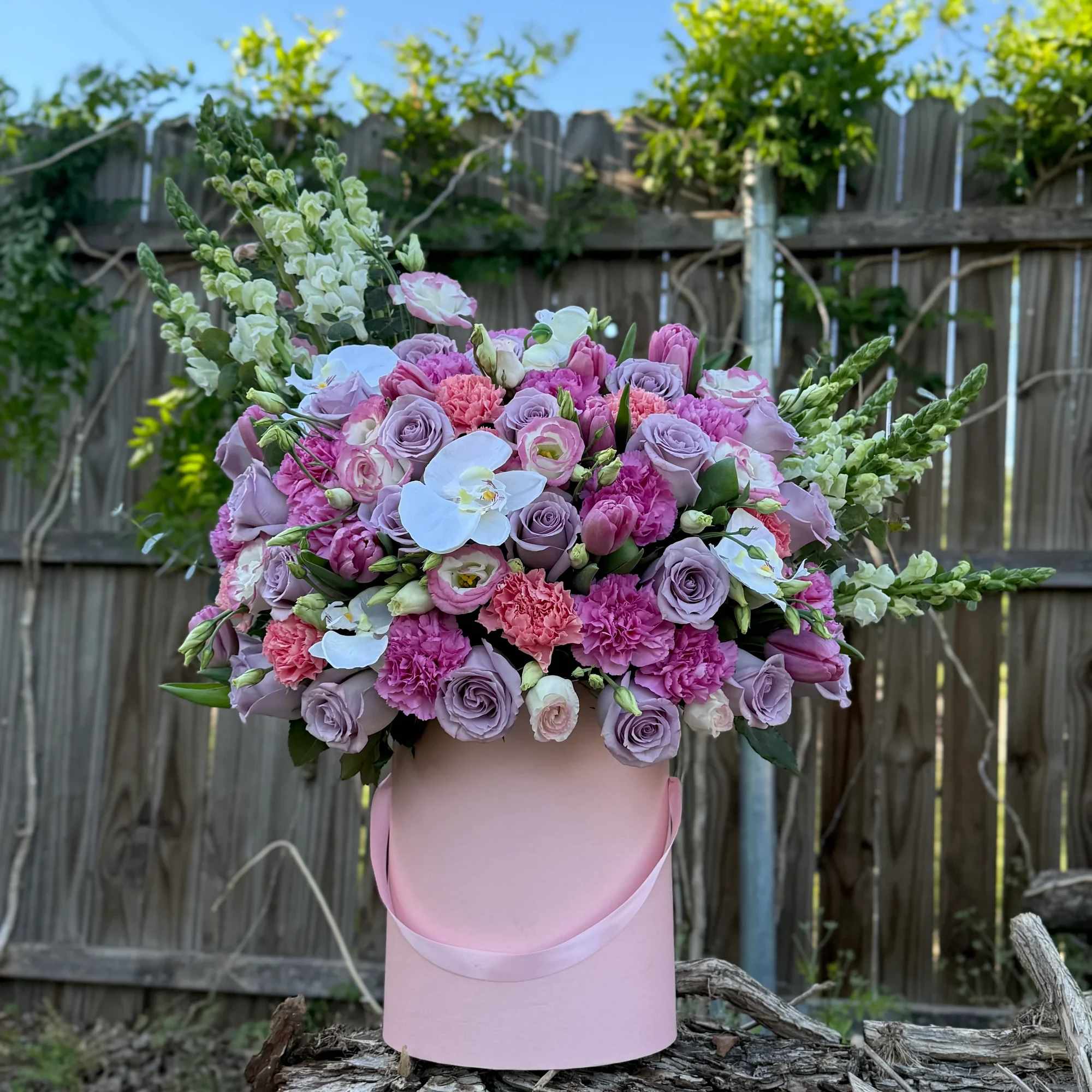 rosas lilas, tonos rosados vibrantes y delicadas orqu&iacute;deas blancas, creando una pieza