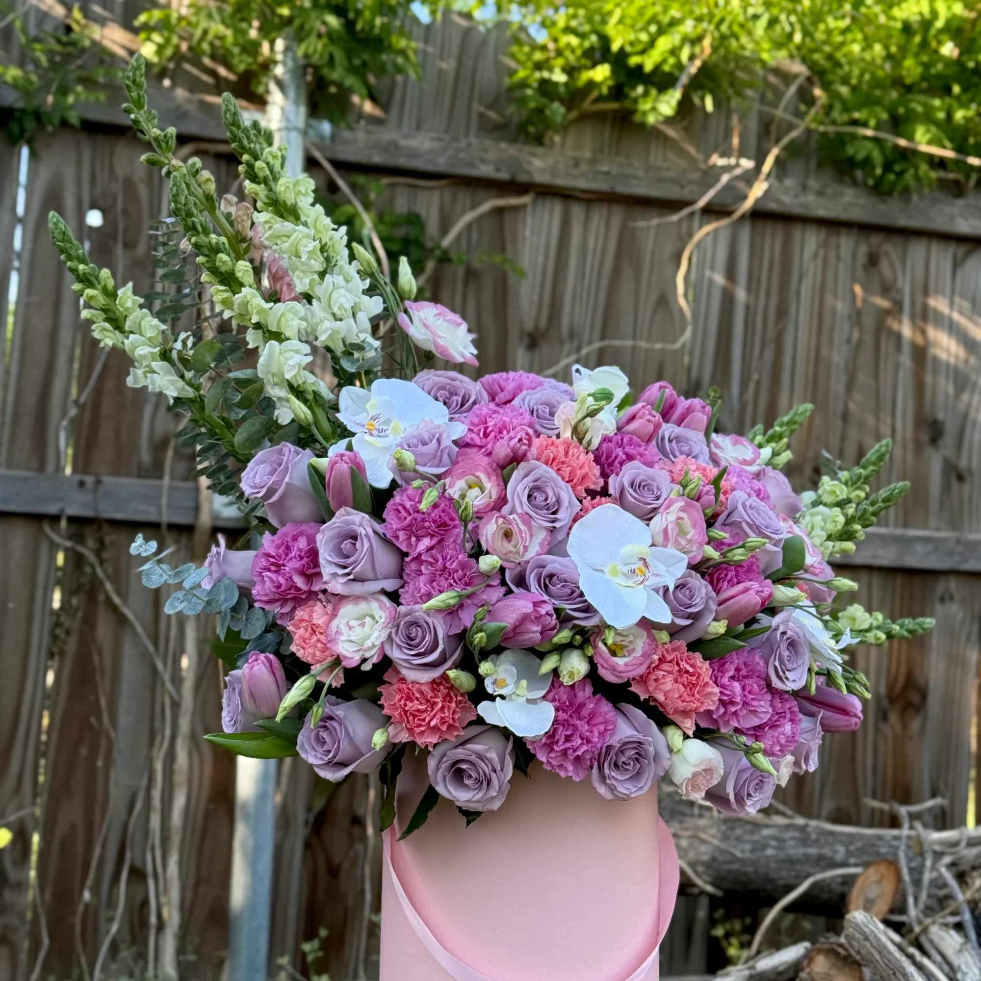rosas lilas, tonos rosados vibrantes y delicadas orqu&iacute;deas blancas, creando una pieza