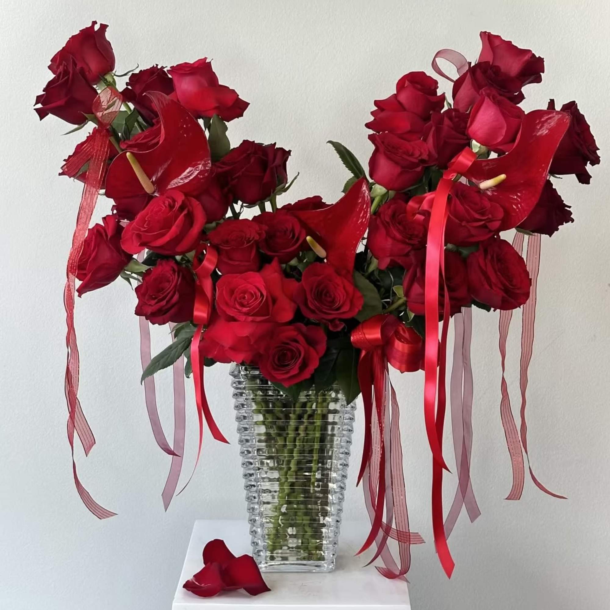 Red roses arranged in a clear ribbed vase with red ribbons