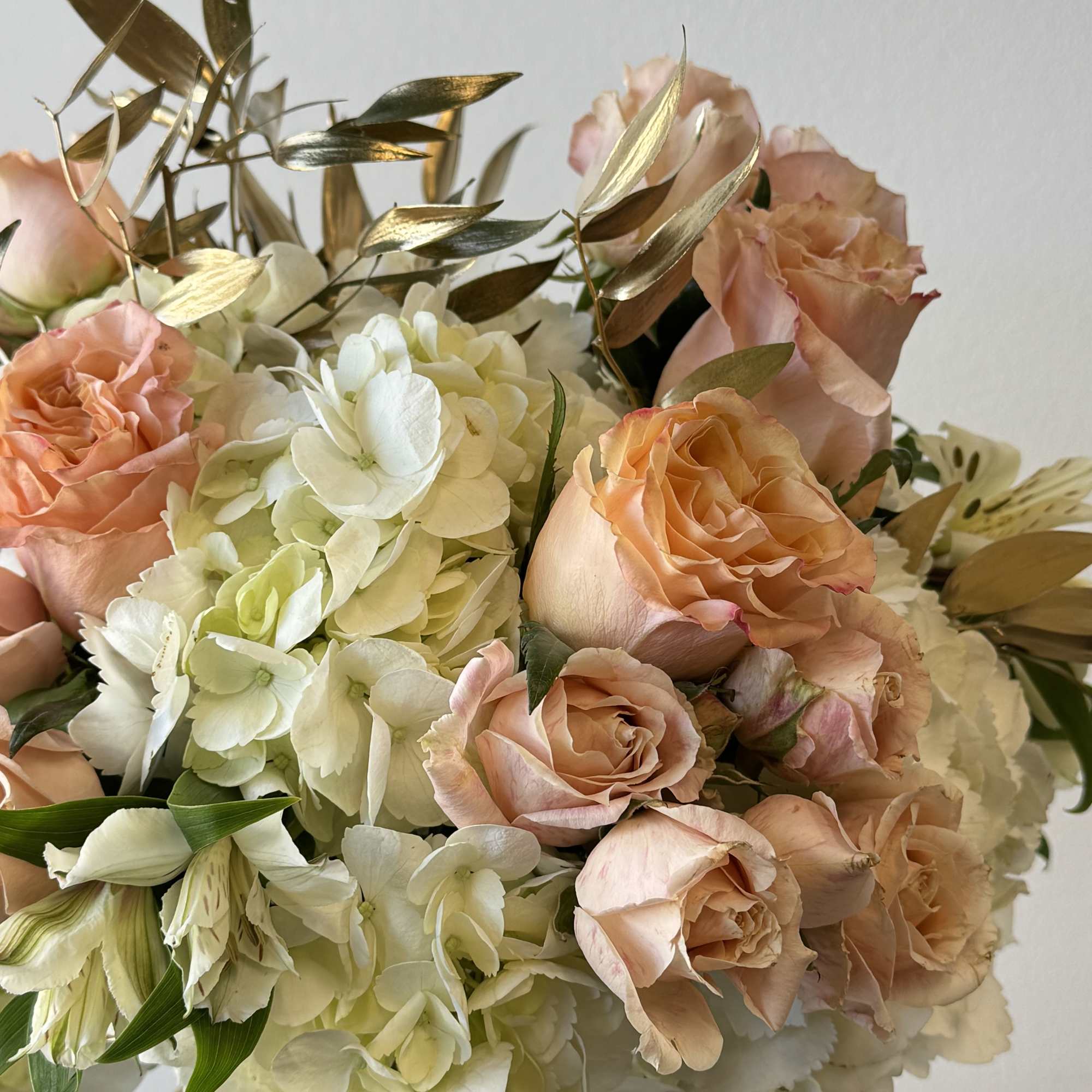 Peach roses and white hydrangeas in a vase with gold foliage