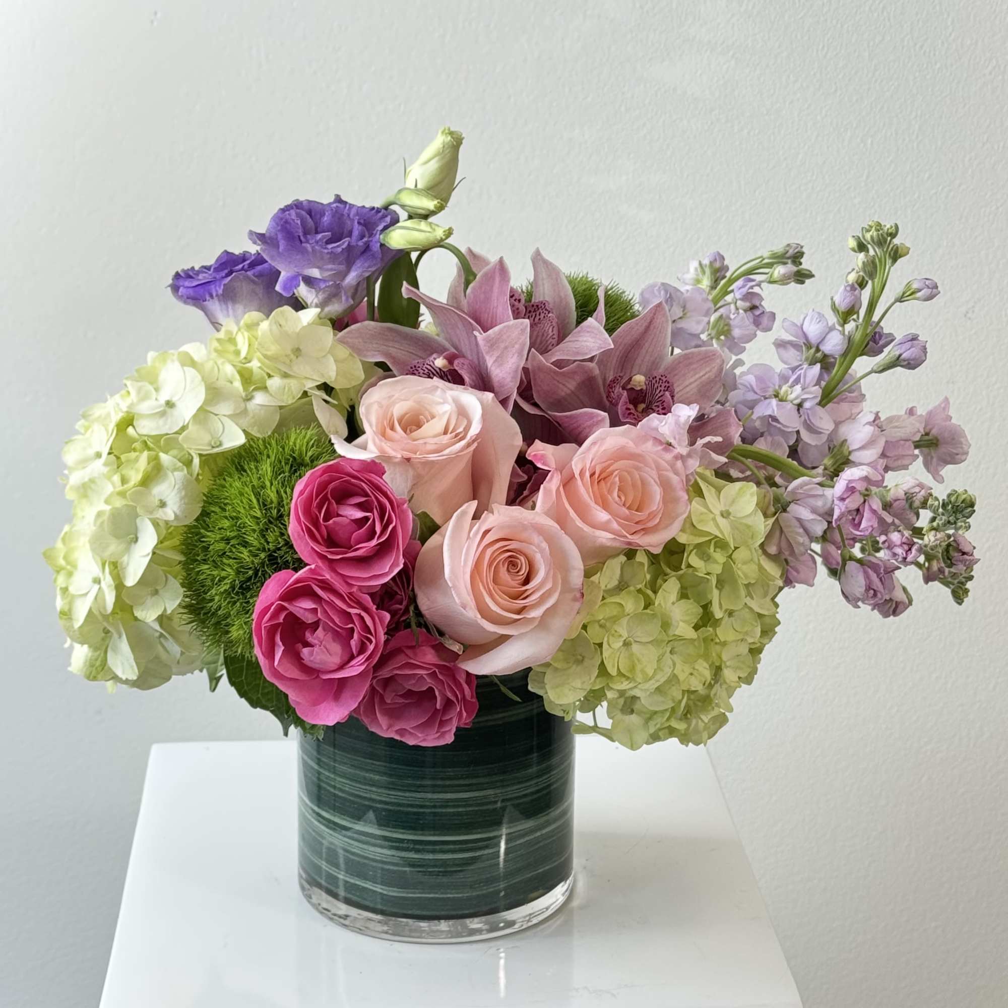 Mixed pink, purple, and green flowers arranged in a glass vase.