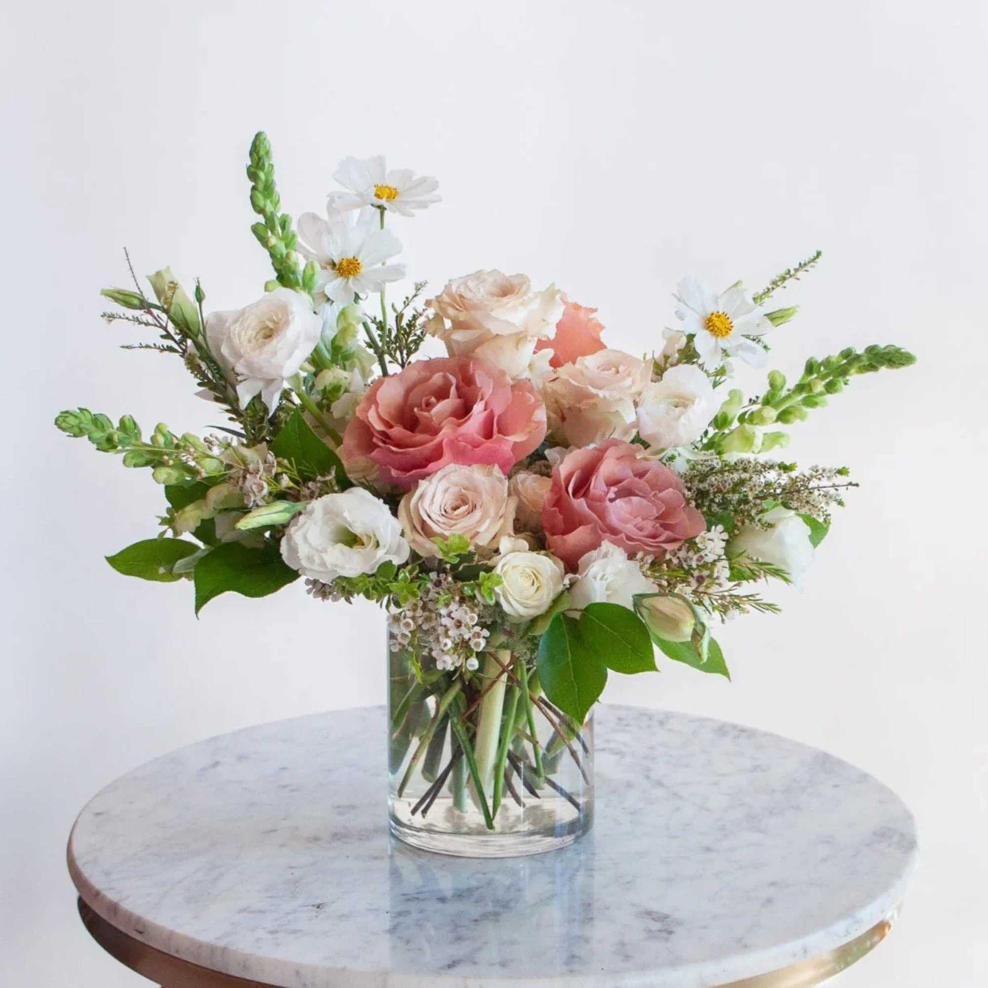 Pink and white roses in a clear glass vase with small white daisies