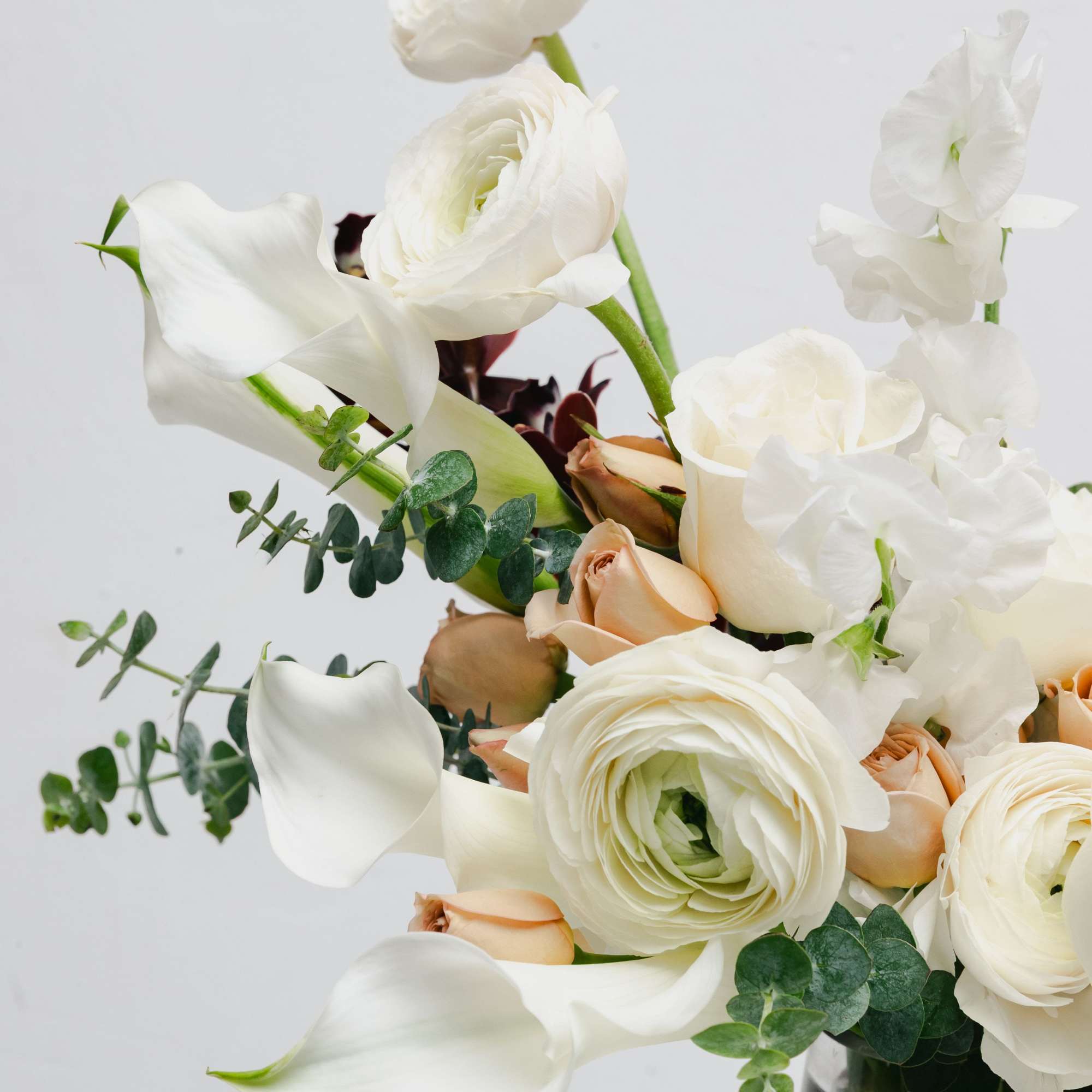 White calla lilies, ranunculus, and pale peach roses in a glass vase