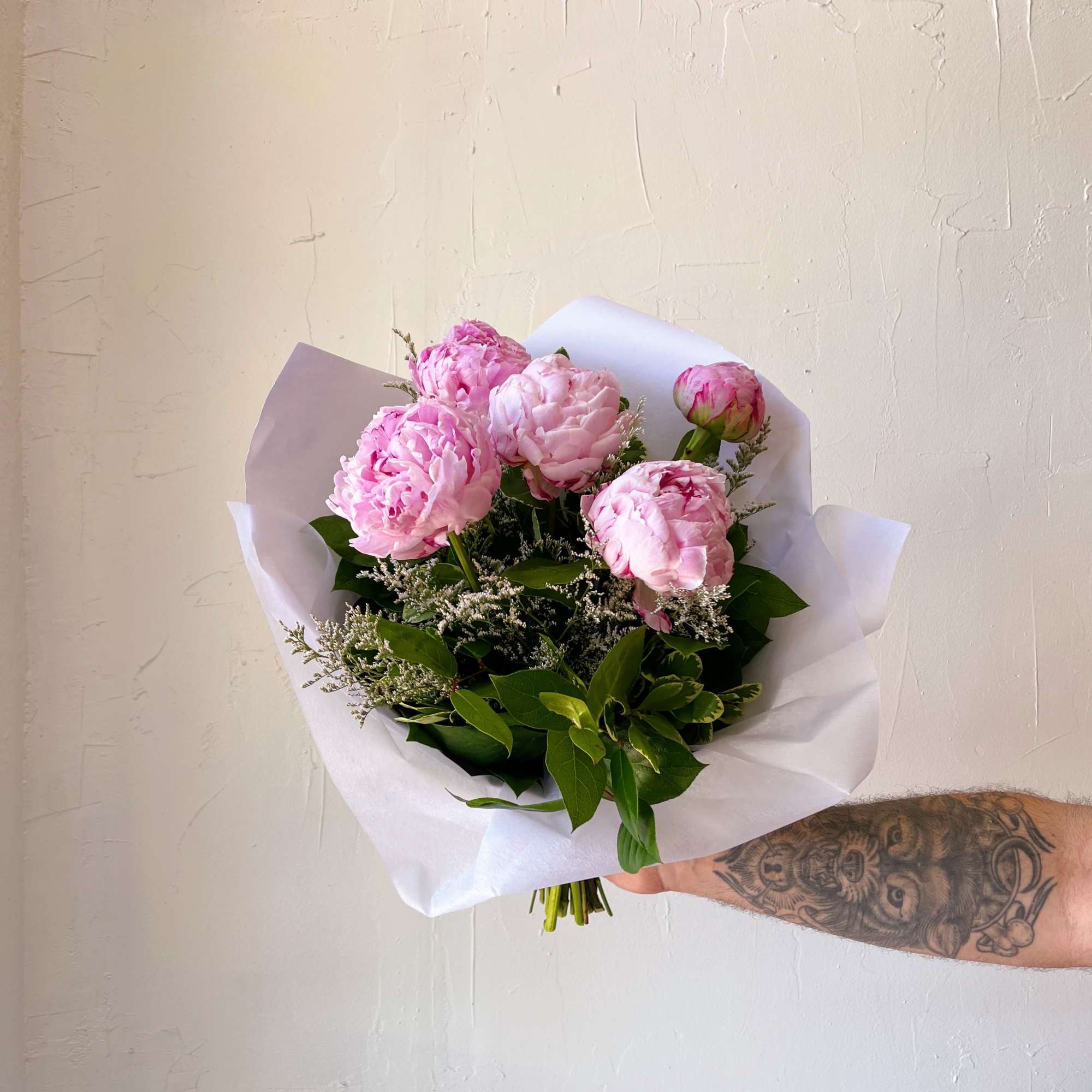 Handheld bouquet of pink peonies wrapped in white paper