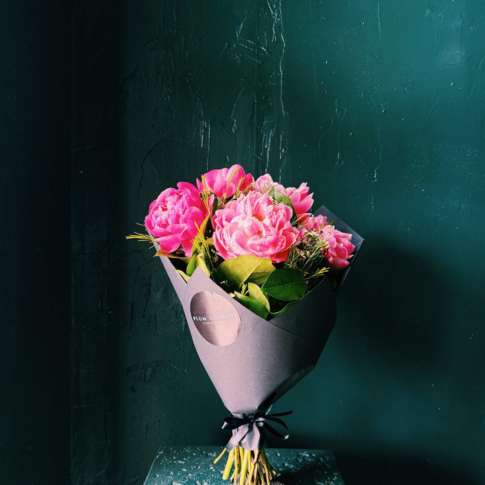 Pink peony bouquet wrapped in dark paper with a black ribbon