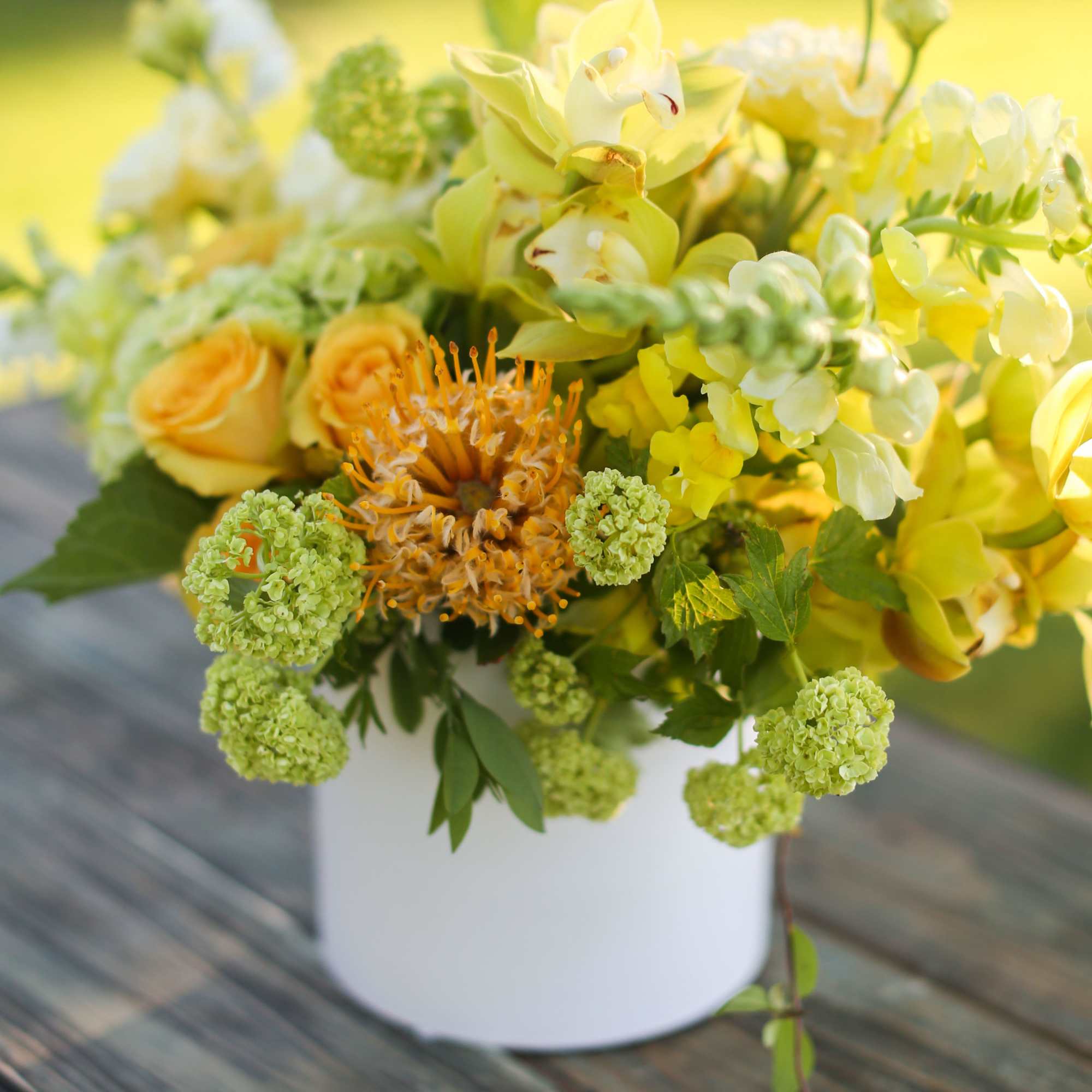 Yellow and green floral arrangement in a white container