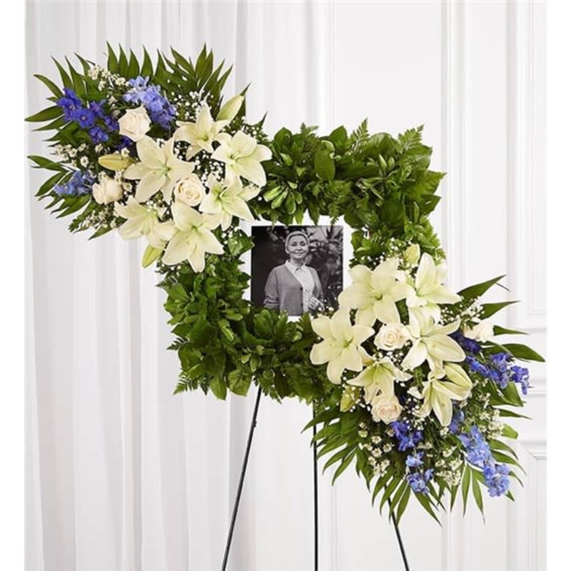 Floral funeral wreath with white lilies and blue flowers around a photo