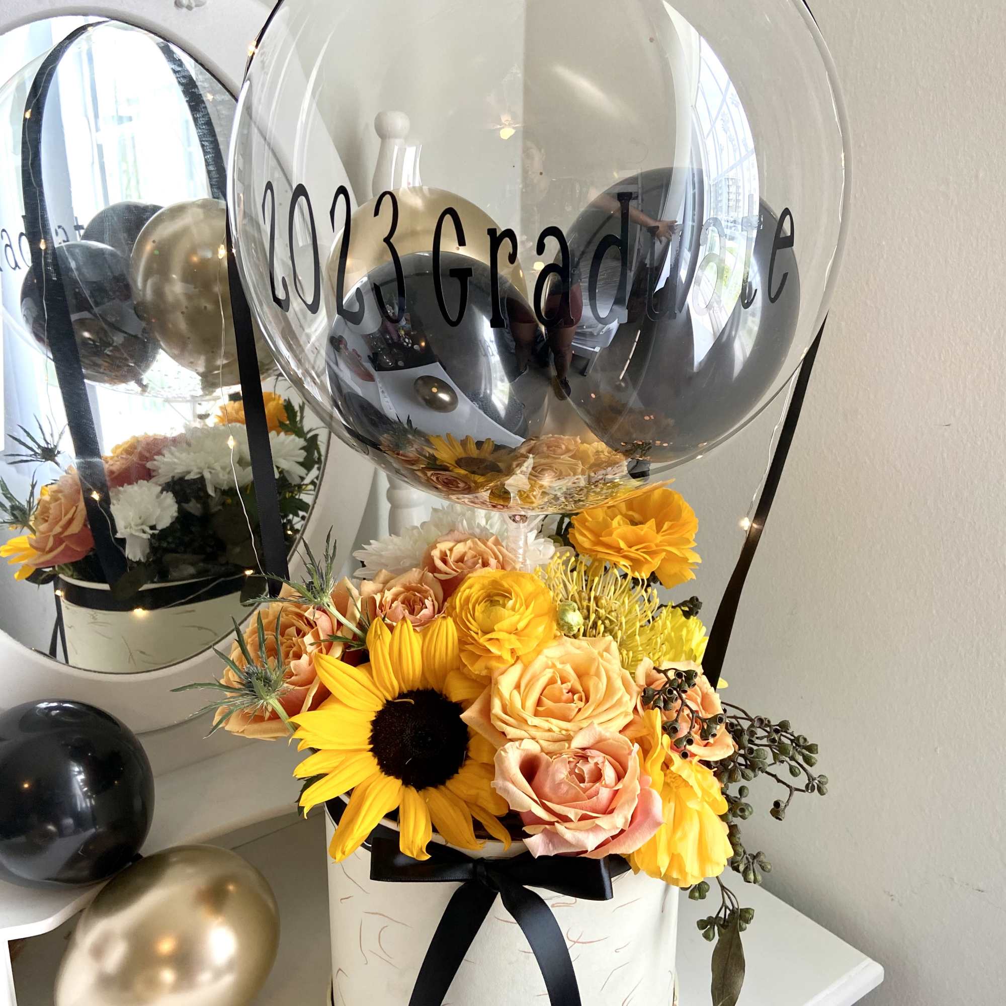 Graduation balloon arrangement with yellow and peach flowers in a hatbox
