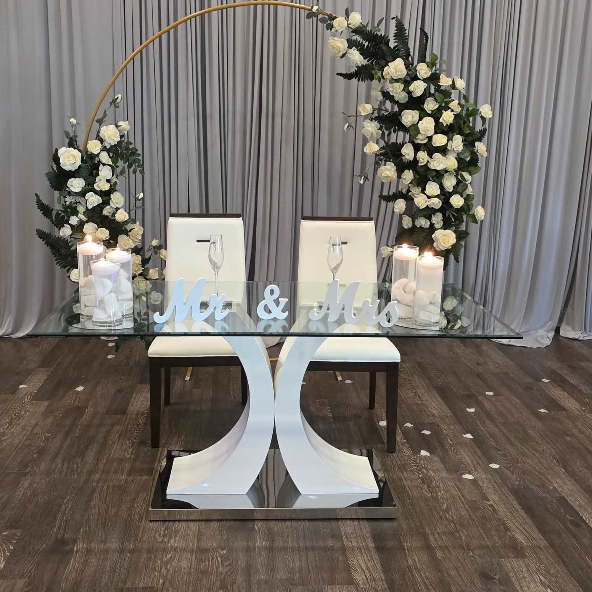 White rose arch over a glass table with candles and "Mr & Mrs" sign