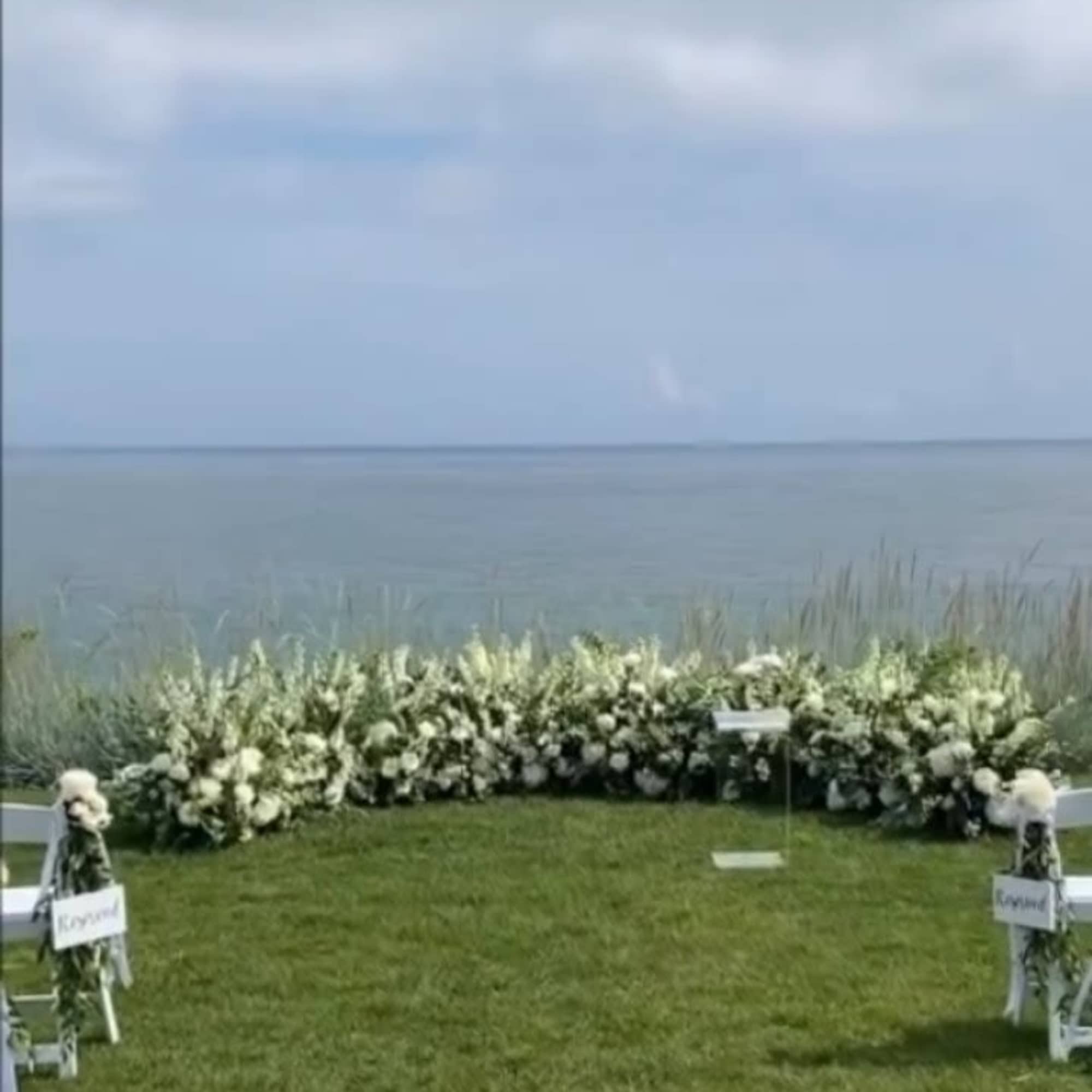 White floral wedding arch on a grassy lawn by the water