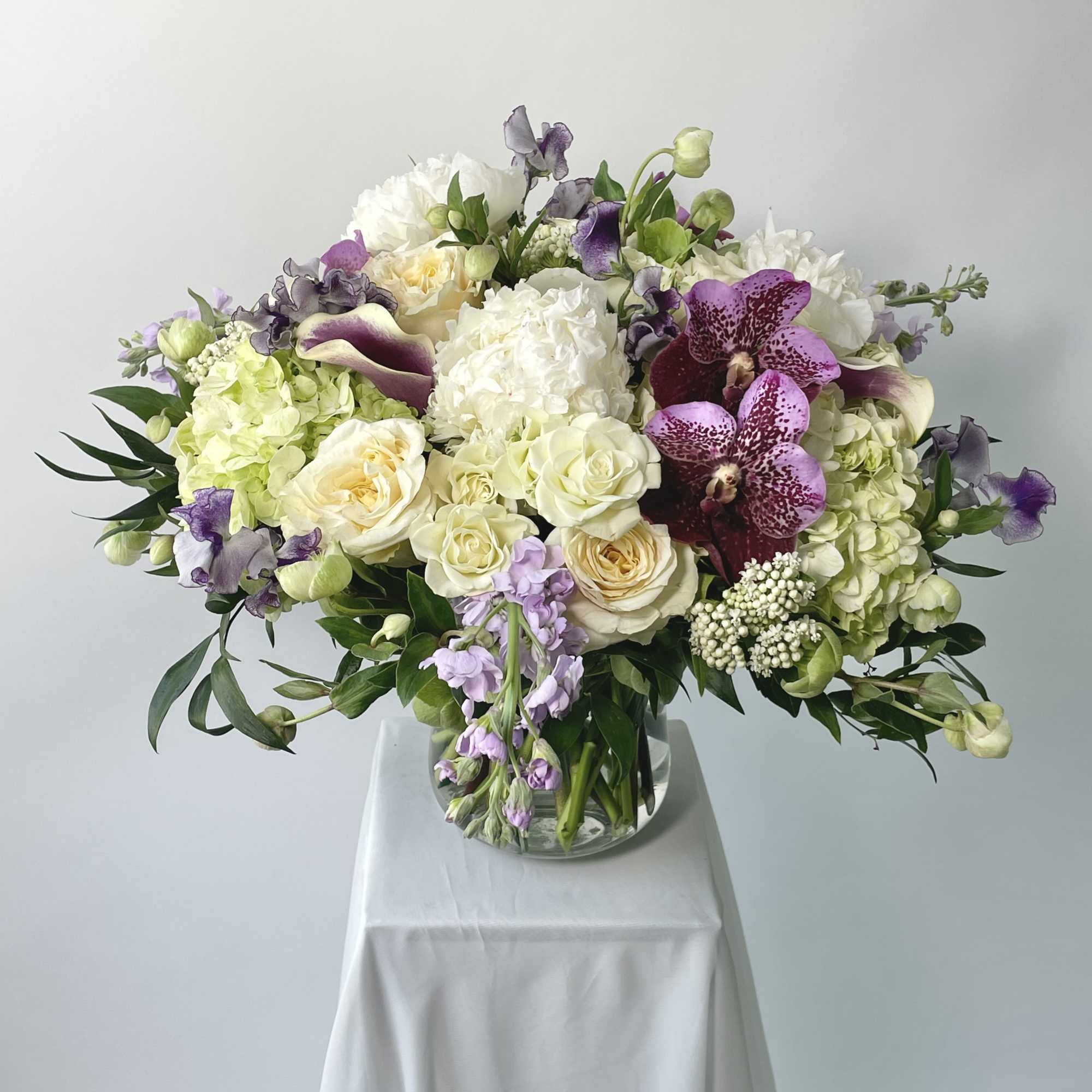 Large bouquet of white, cream, and purple flowers in a glass vase