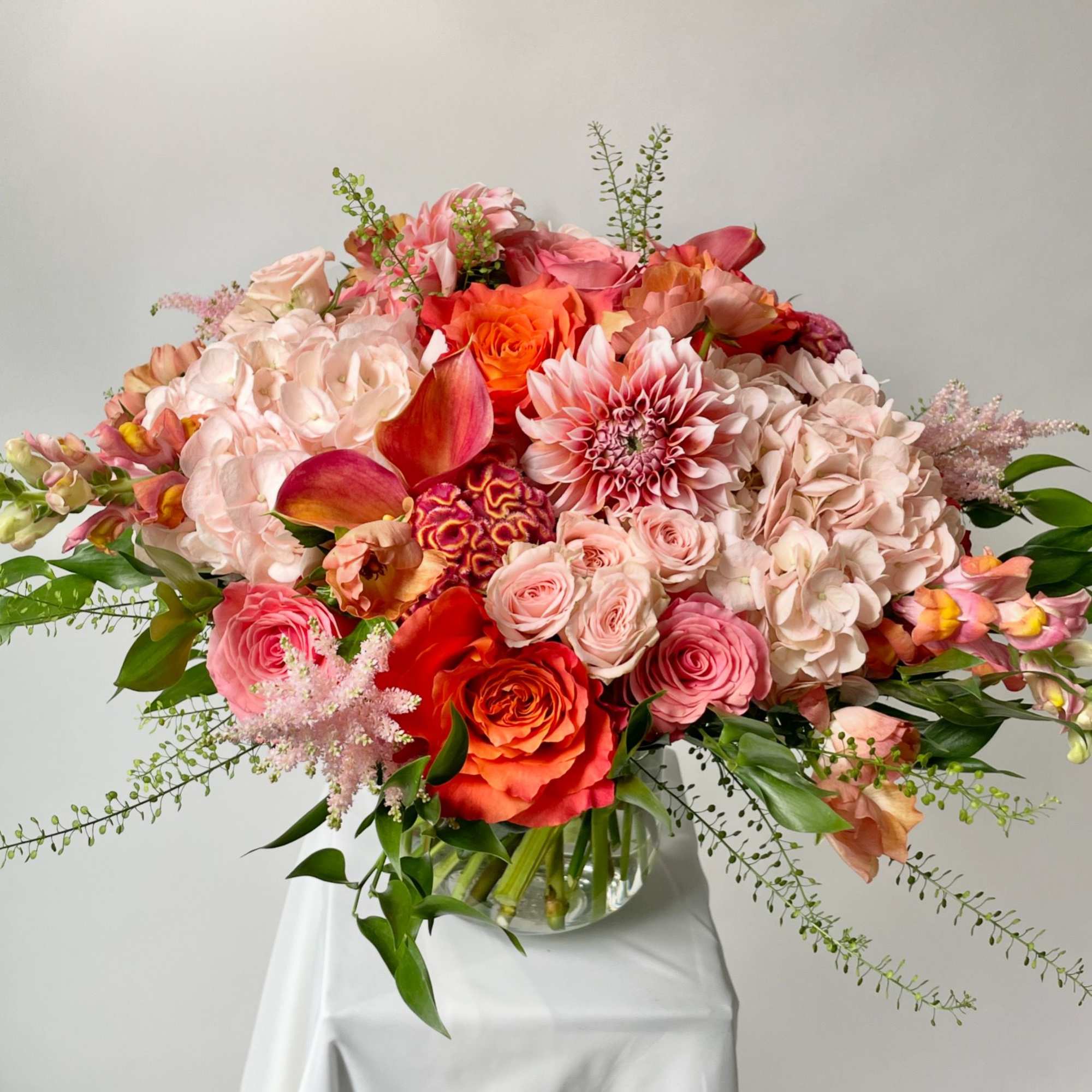 Large mixed bouquet of pink, peach, and orange flowers in a glass vase
