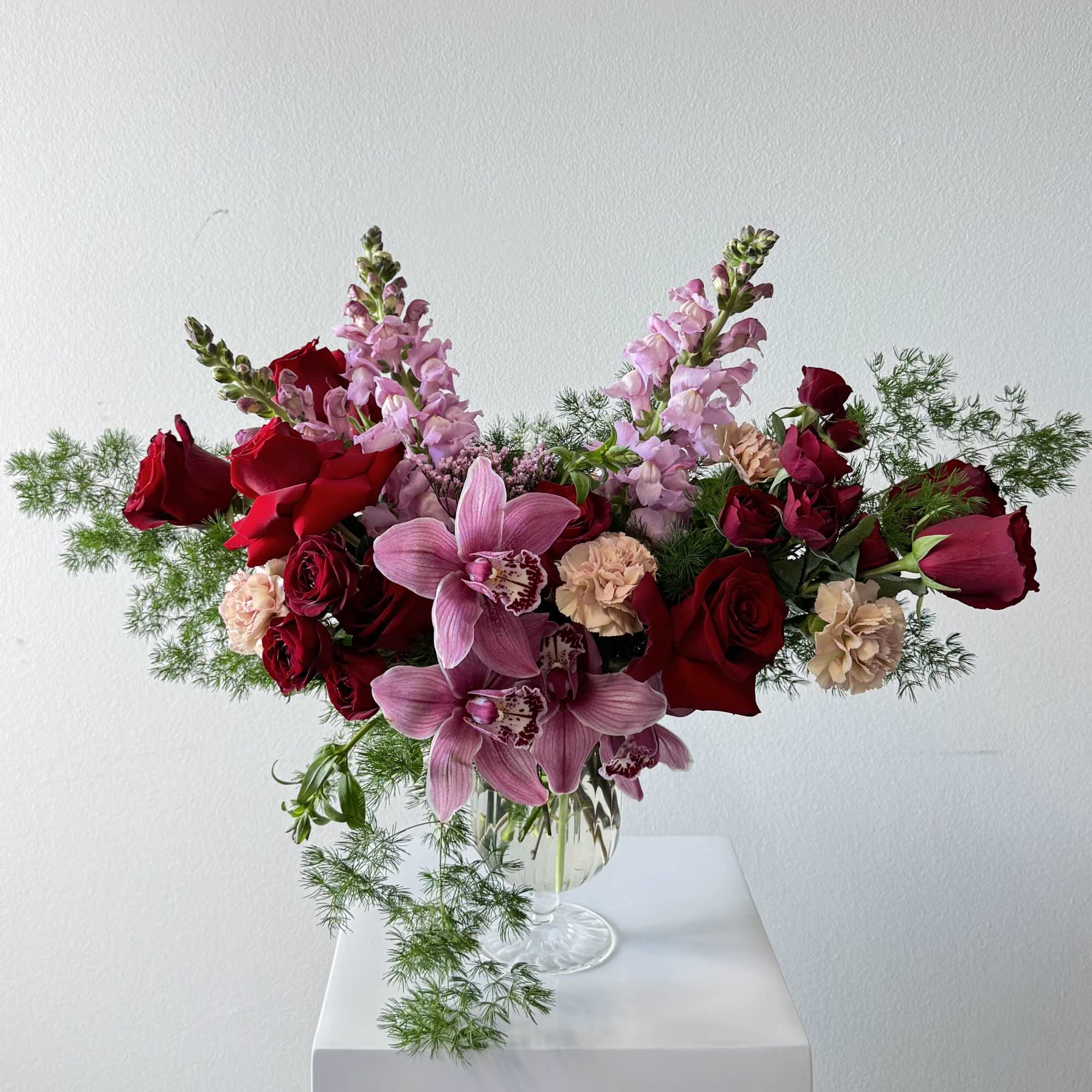 Pink orchids and red roses arranged in a clear glass vase