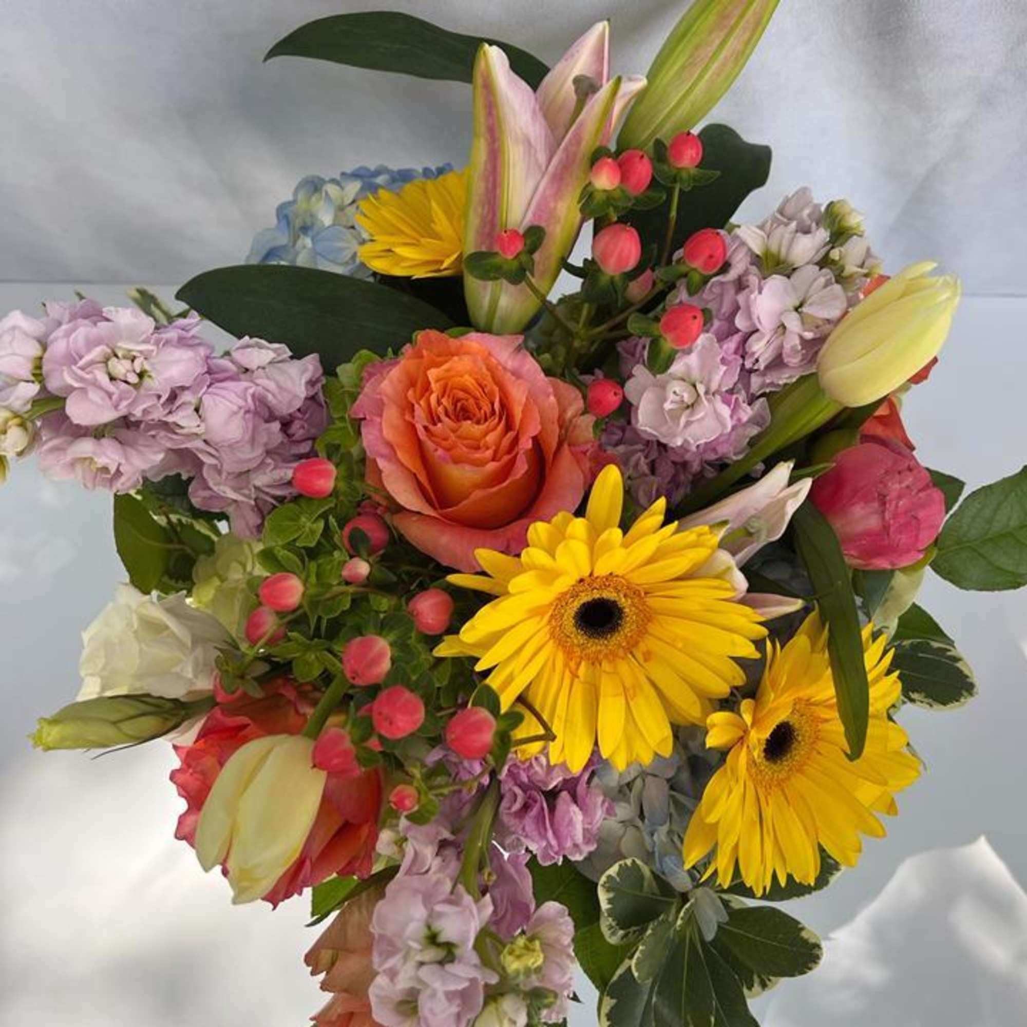 Colorful mixed bouquet with yellow gerbera daisies, orange rose, lilies, tulips, and pastel stock flowers