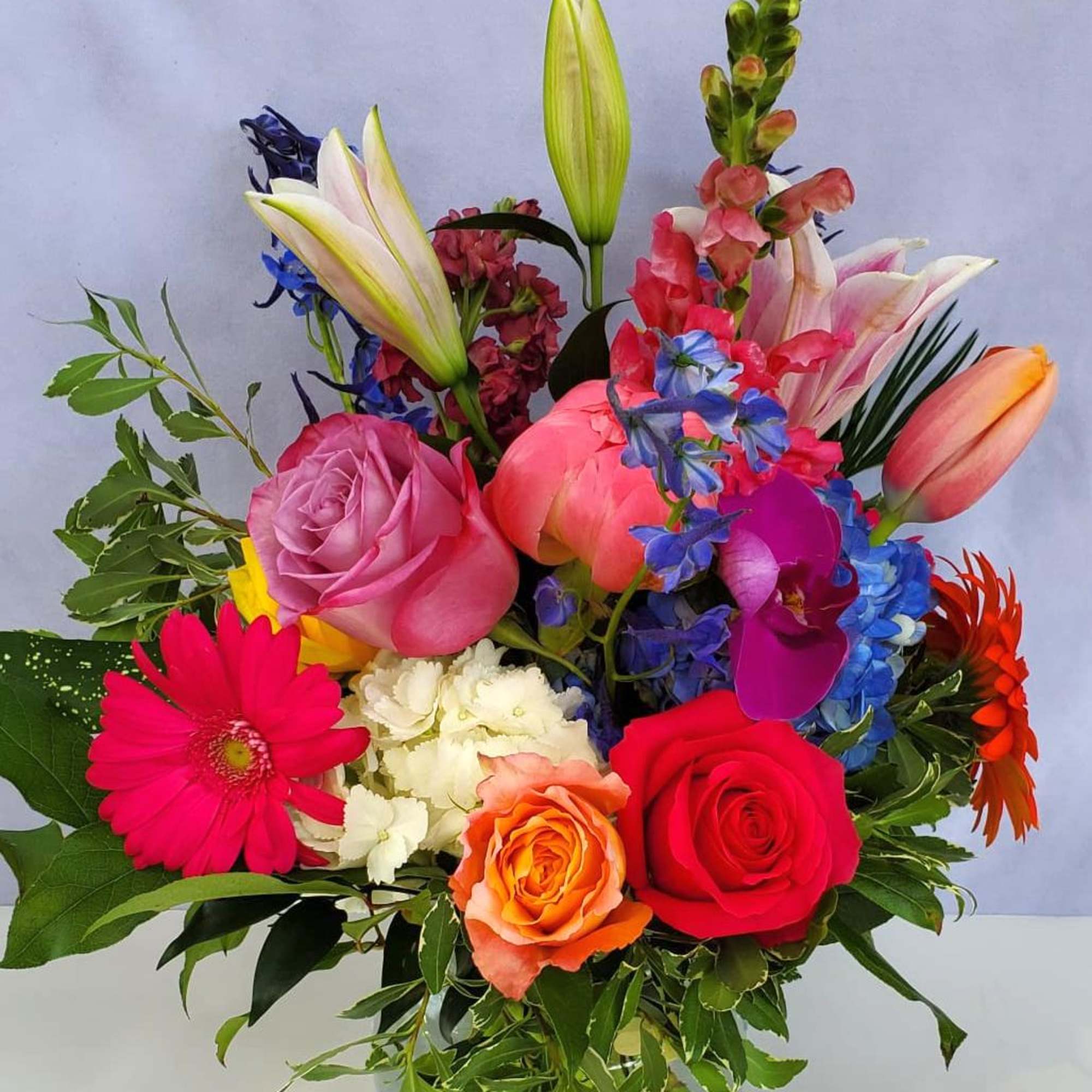 Bright mixed bouquet of roses, lilies, gerberas, tulips, orchids and other flowers in a clear glass bowl vase