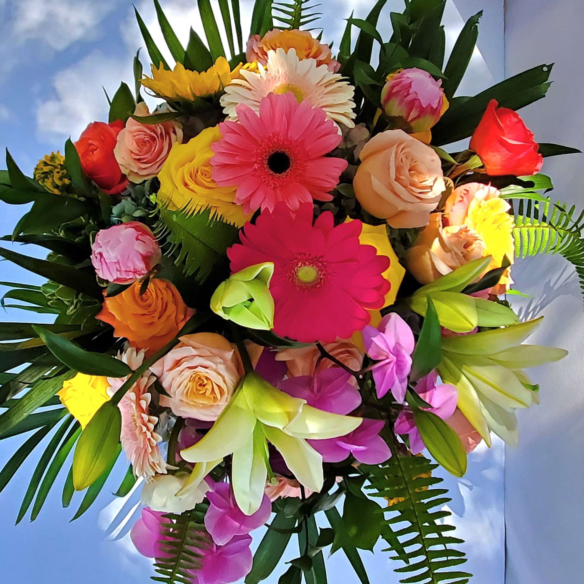 Bright mixed bouquet of pink gerbera daisies, roses, lilies, and orchids in vivid warm colors