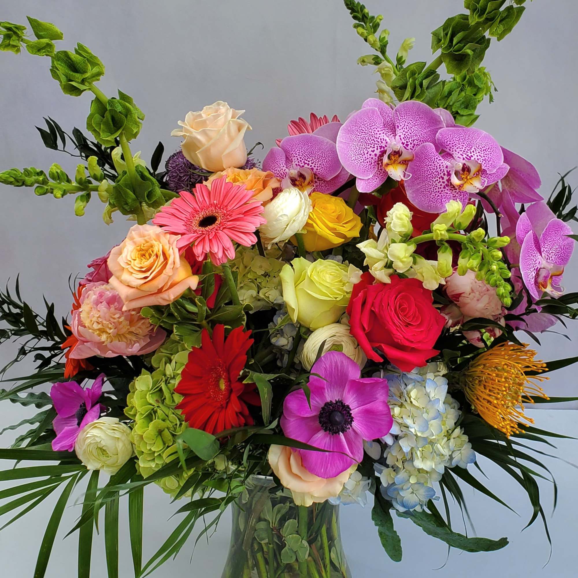 Large multicolored arrangement of roses, orchids, gerberas, and hydrangeas in a clear glass vase