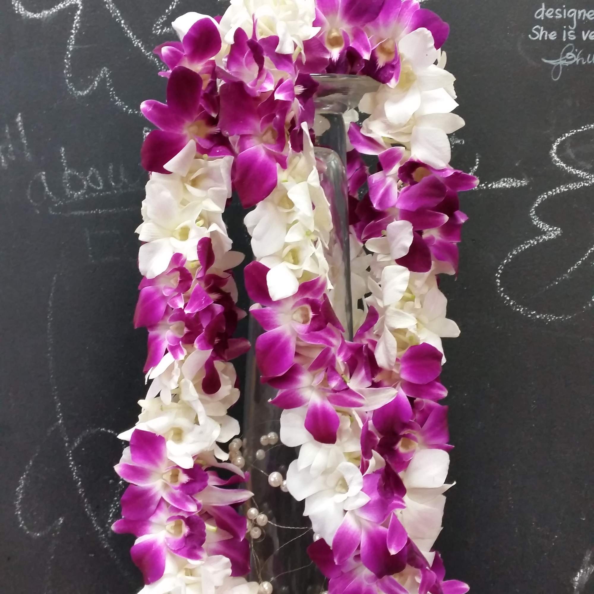Purple and white orchid lei draped over a glass vase