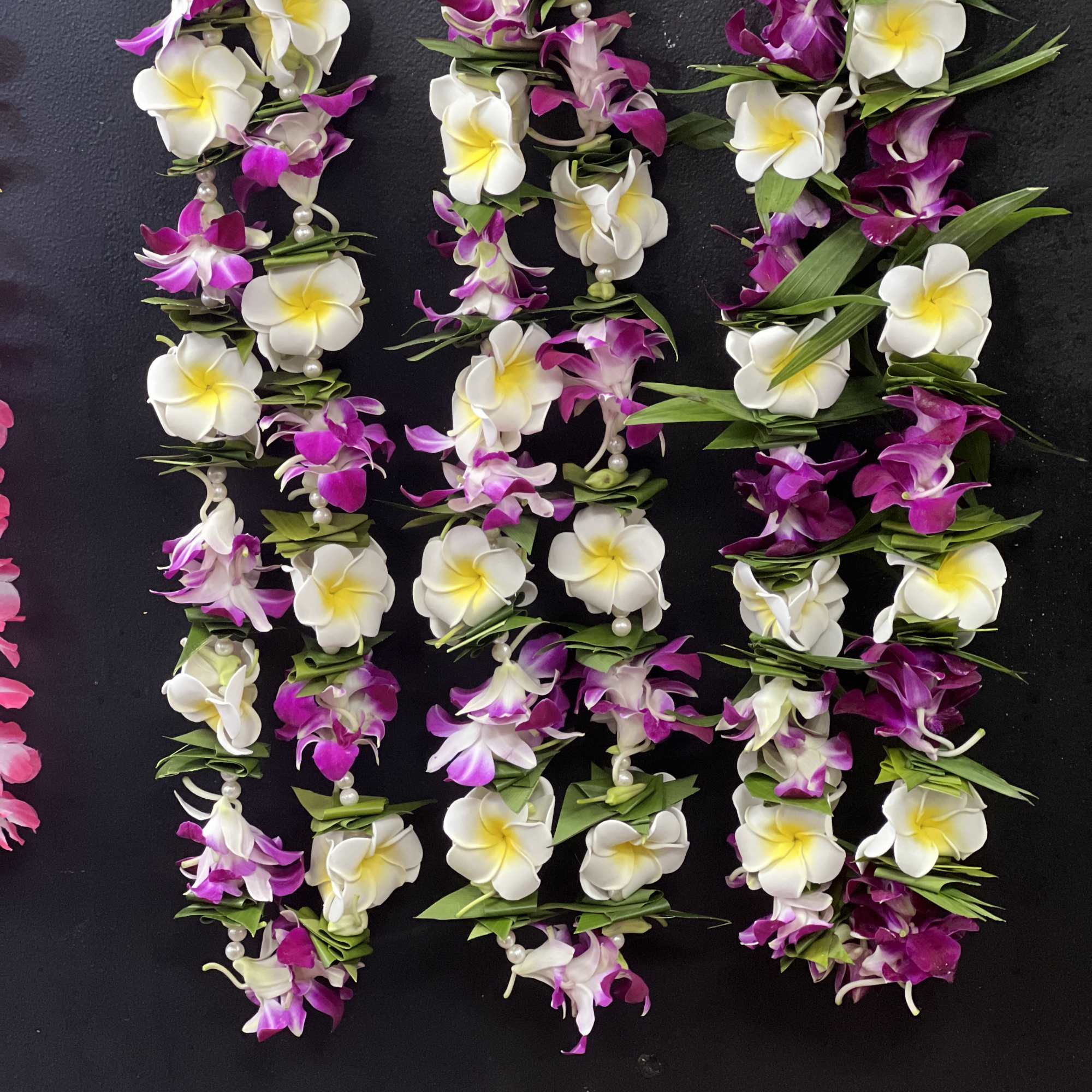 Three purple and white flower leis with pearl accents on a dark background