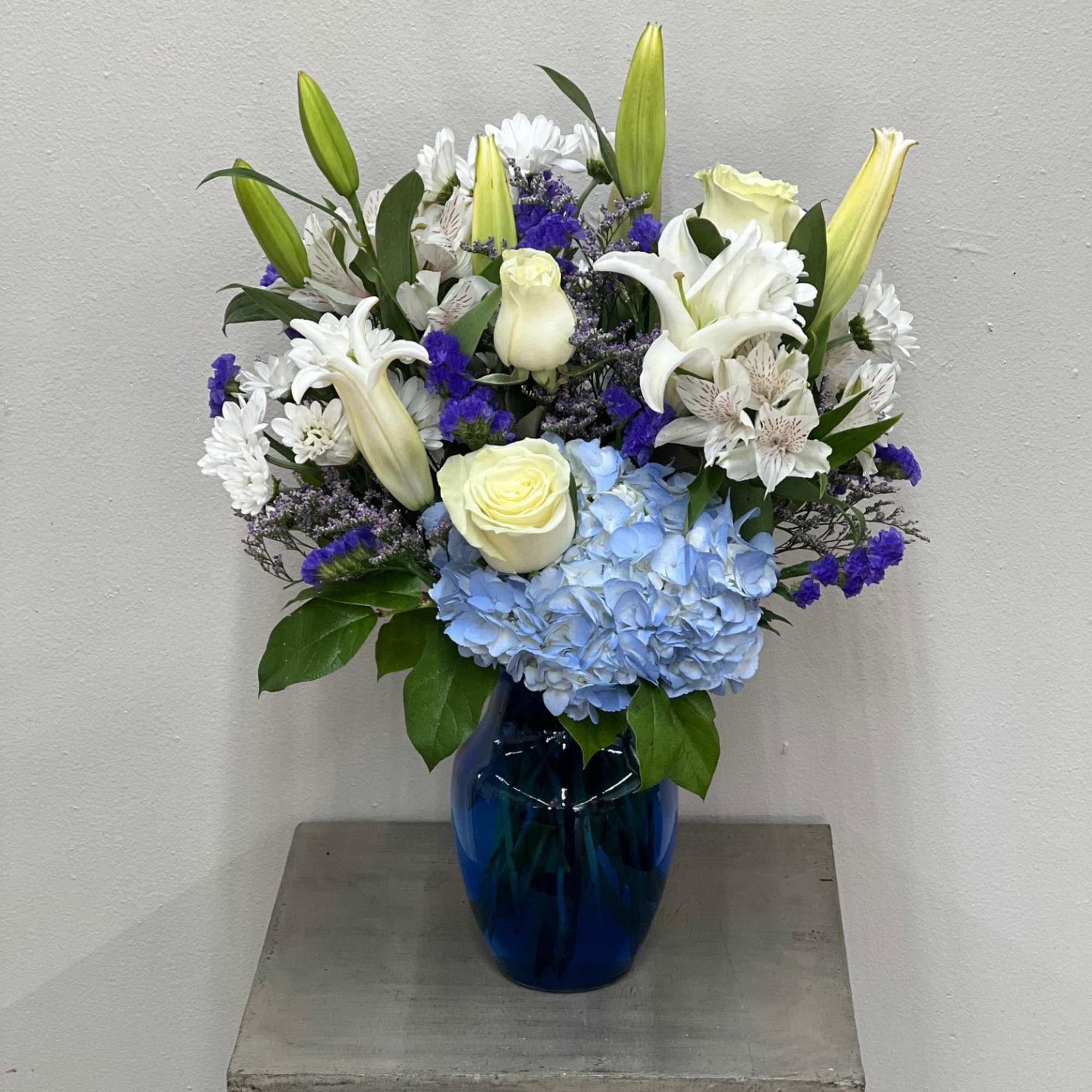 Blue vase with white lilies, roses, hydrangea, and purple accents