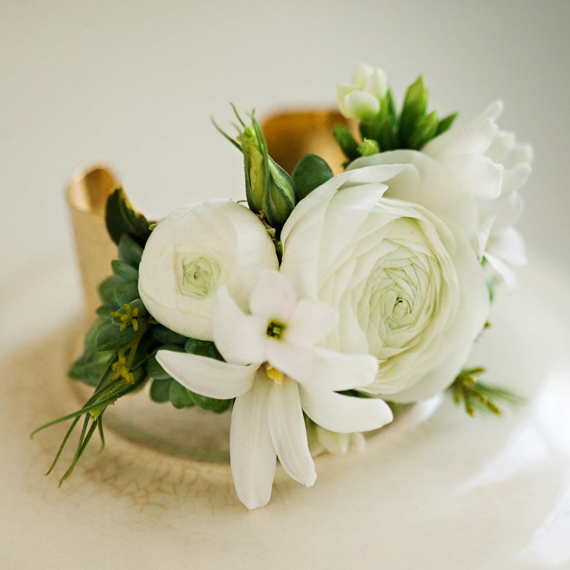 Cuff corsage featuring ranunculus with bits of foliage and other filler flowers.