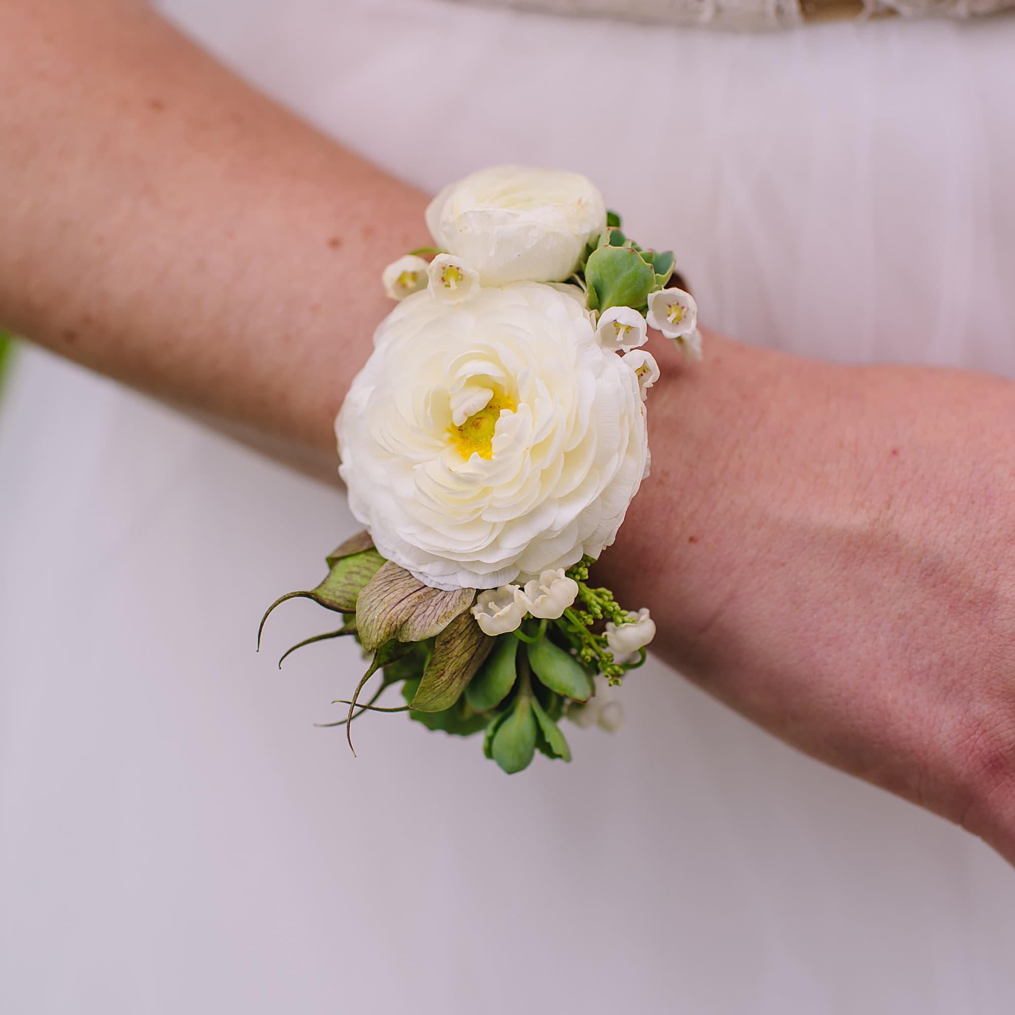 Cuff corsage featuring ranunculus with bits of foliage and other filler flowers.